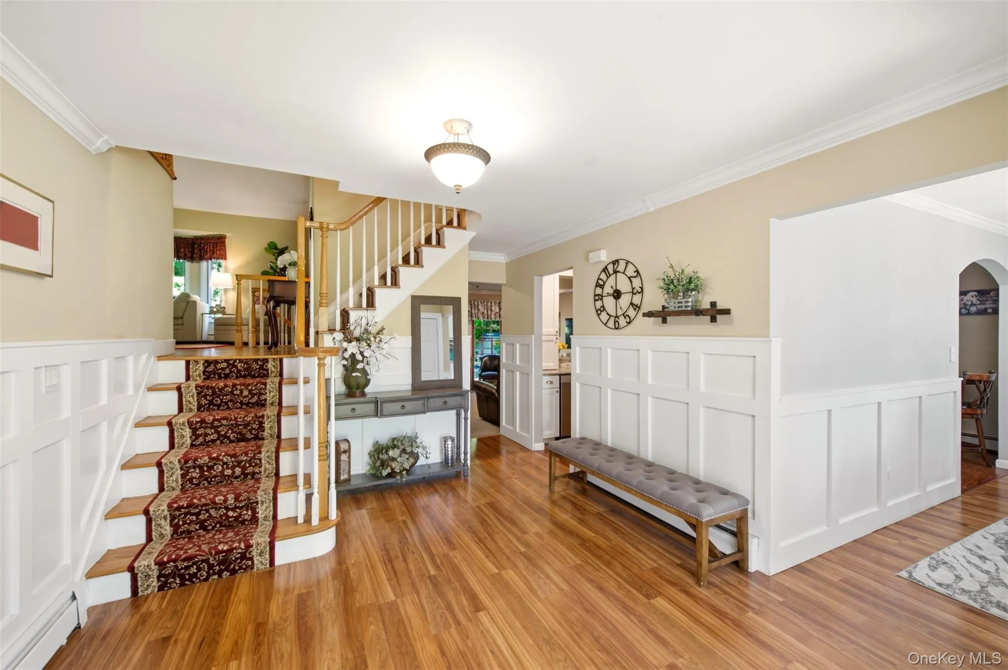 Wood-finish flooring, white wainscoting, crown molding, and a chandelier-style ceiling light Wood-finish flooring, white wainscoting, crown molding, and a chandelier-style ceiling light