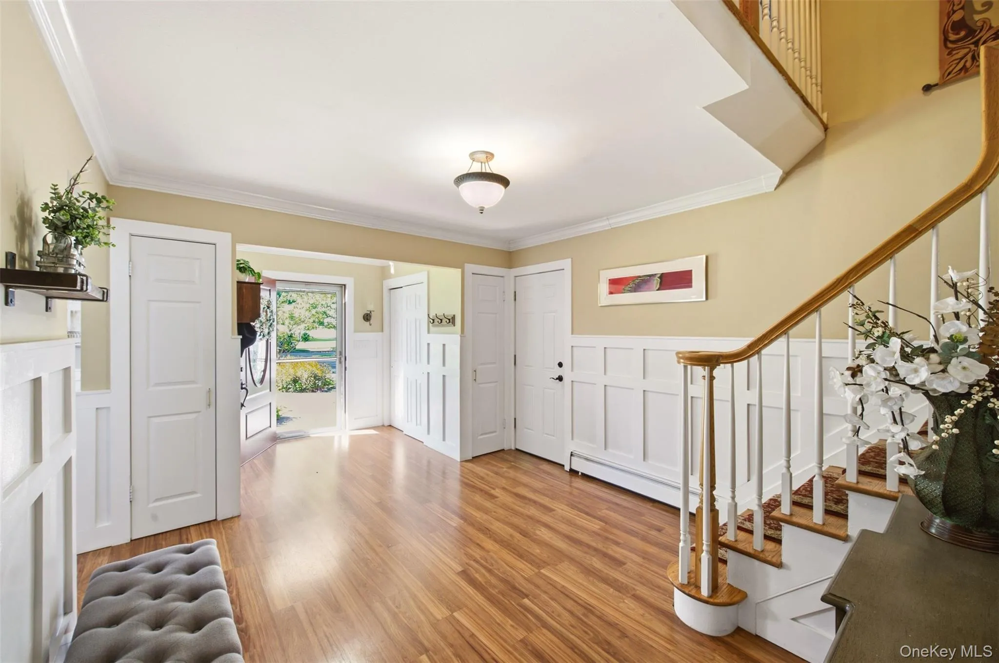Hardwood-finish flooring, white wainscoting, crown molding, open staircase with wood handrail, and a semi-flush mount ceiling light Hardwood-finish flooring, white wainscoting, crown molding, open staircase with wood handrail, and a semi-flush mount ceiling light