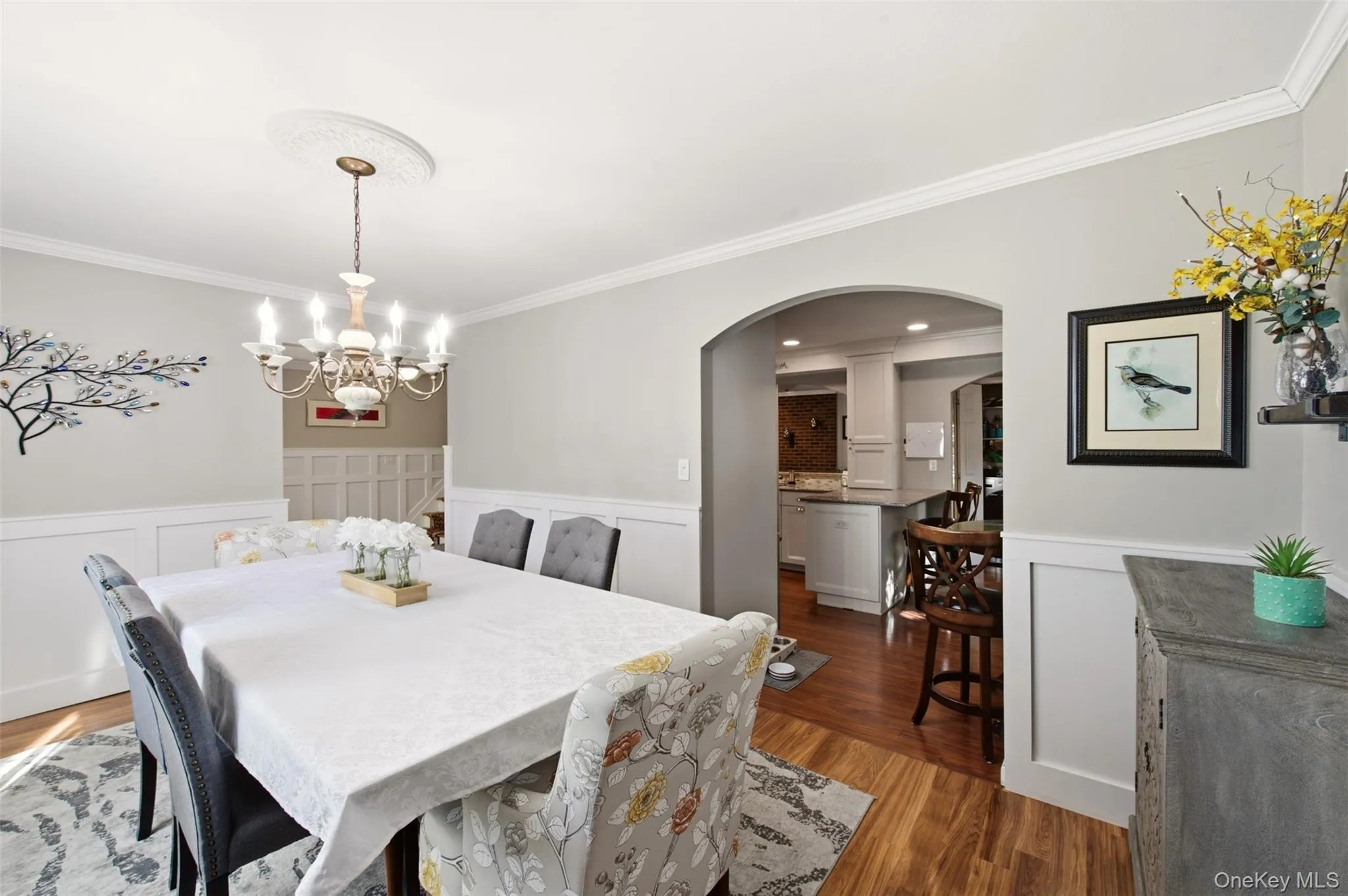 Hardwood-finish flooring, crown molding, wainscoting, an arched doorway, and a chandelier with a ceiling medallion Hardwood-finish flooring, crown molding, wainscoting, an arched doorway, and a chandelier with a ceiling medallion