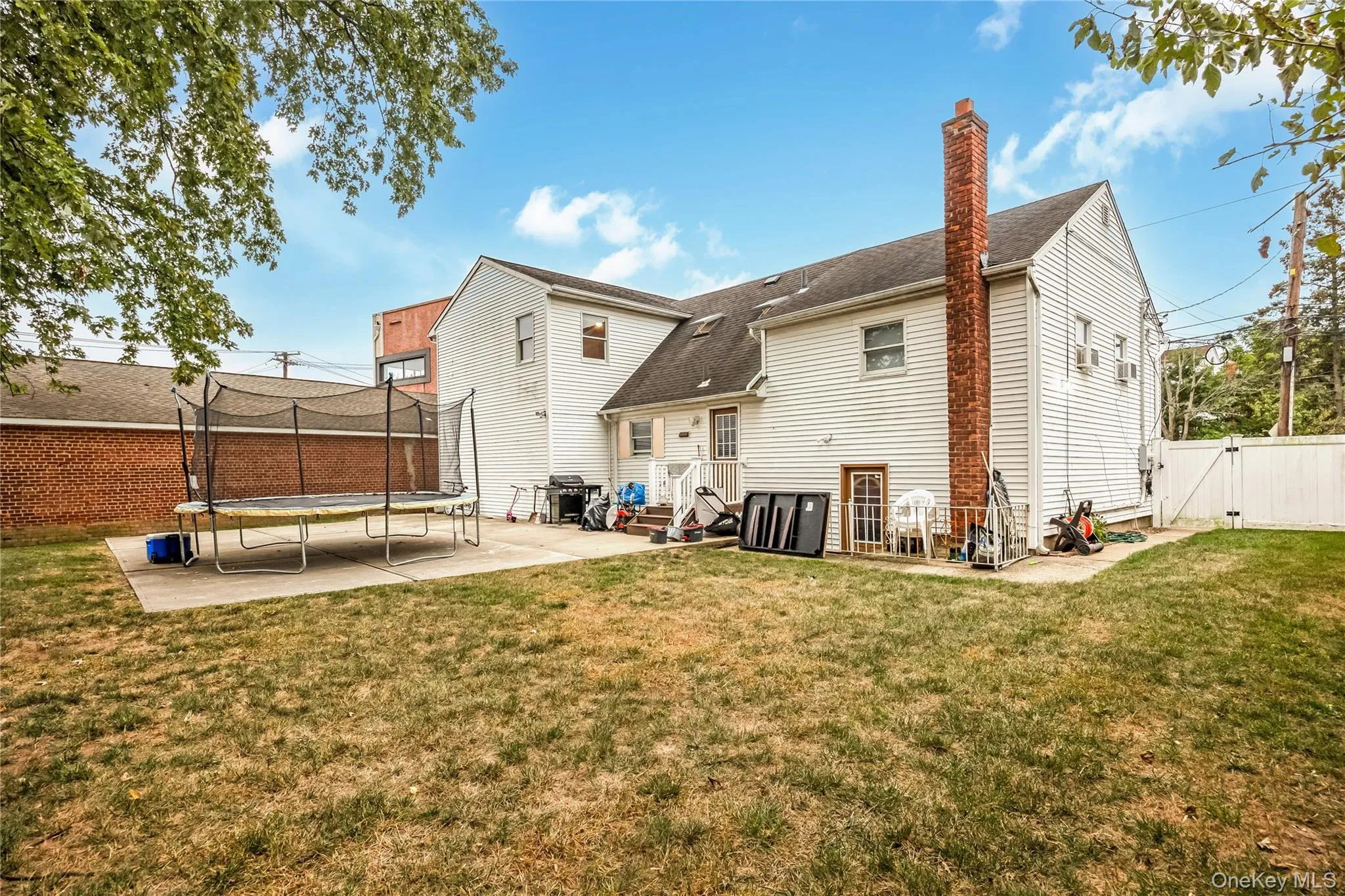 Rear view of property featuring a patio, a gate, a trampoline, a chimney, and a shingled roof Rear view of property featuring a patio, a gate, a trampoline, a chimney, and a shingled roof