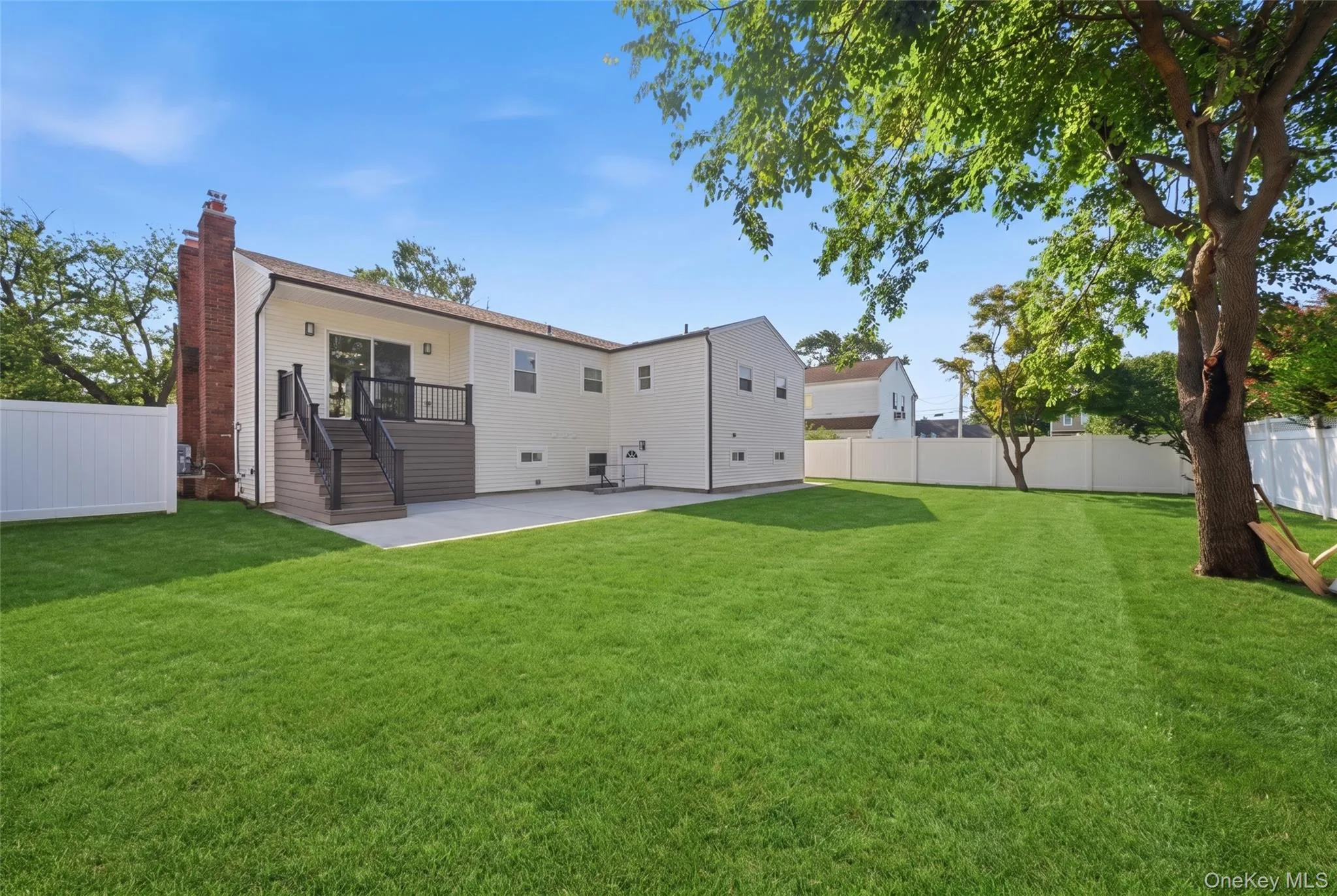 Expansive grass area with a privacy fence, an elevated deck, and a concrete patio Expansive grass area with a privacy fence, an elevated deck, and a concrete patio