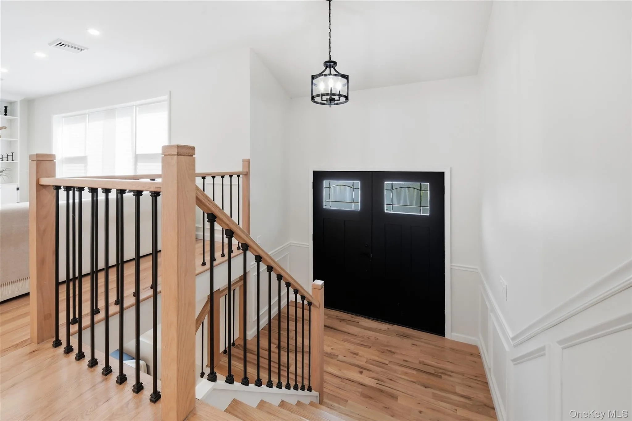 Entryway featuring a paneled double door with leaded glass inserts, wood-finish flooring, a wood and wrought iron staircase, and wainscoting Entryway featuring a paneled double door with leaded glass inserts, wood-finish flooring, a wood and wrought iron staircase, and wainscoting
