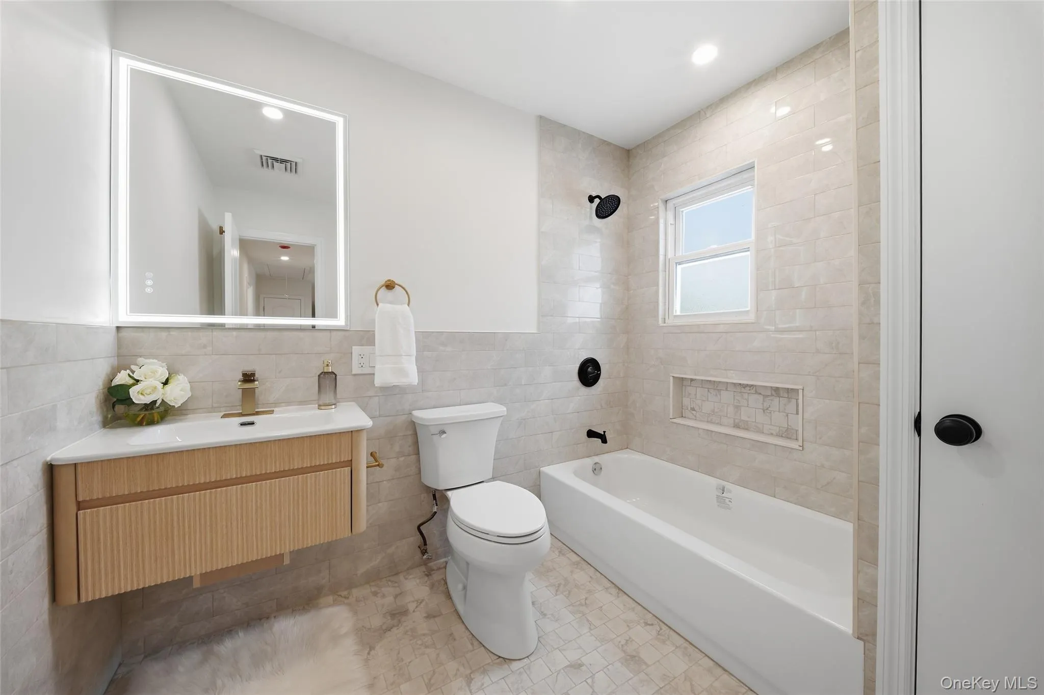 Floating vanity with fluted wood-finish cabinetry, illuminated mirror, and a single basin sink Floating vanity with fluted wood-finish cabinetry, illuminated mirror, and a single basin sink