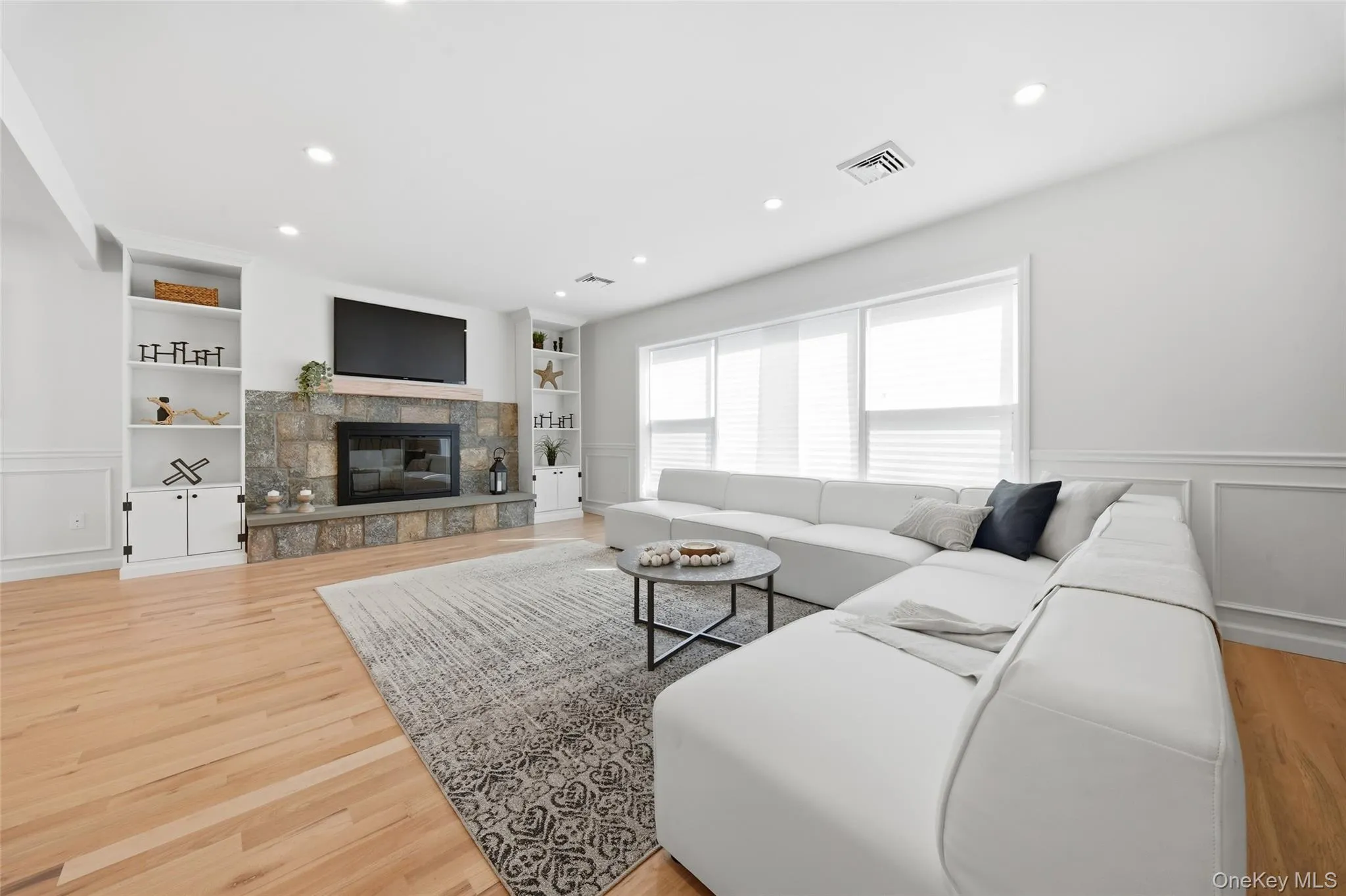 Living area featuring hardwood flooring, recessed lighting, a stone-clad fireplace with built-in shelving, and extensive wainscoting Living area featuring hardwood flooring, recessed lighting, a stone-clad fireplace with built-in shelving, and extensive wainscoting
