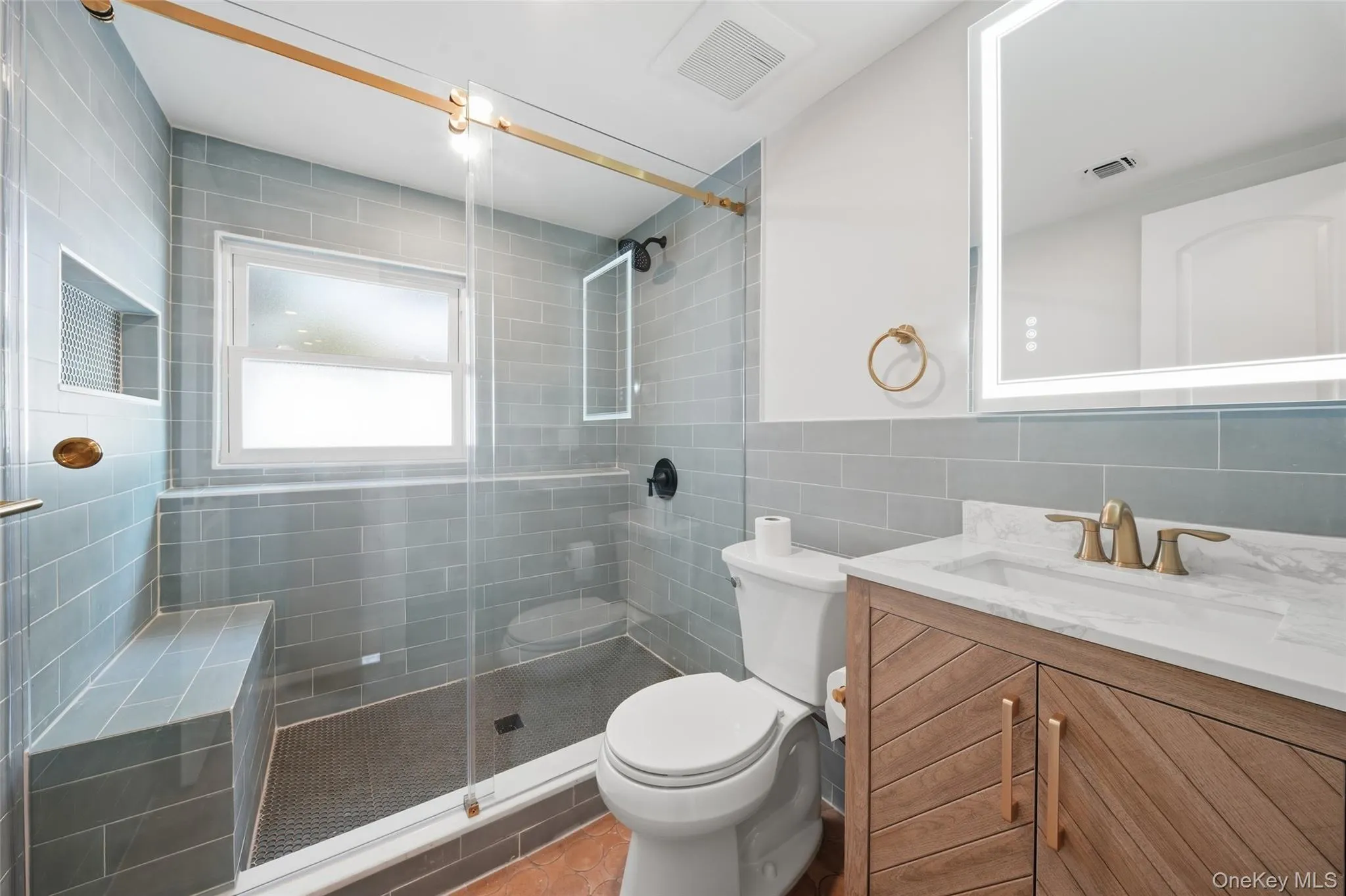 Lower level Curated bathroom featuring a glass-enclosed shower with tiled bench, a wood-finish vanity with a single basin sink, and an illuminated mirror Lower level Curated bathroom featuring a glass-enclosed shower with tiled bench, a wood-finish vanity with a single basin sink, and an illuminated mirror