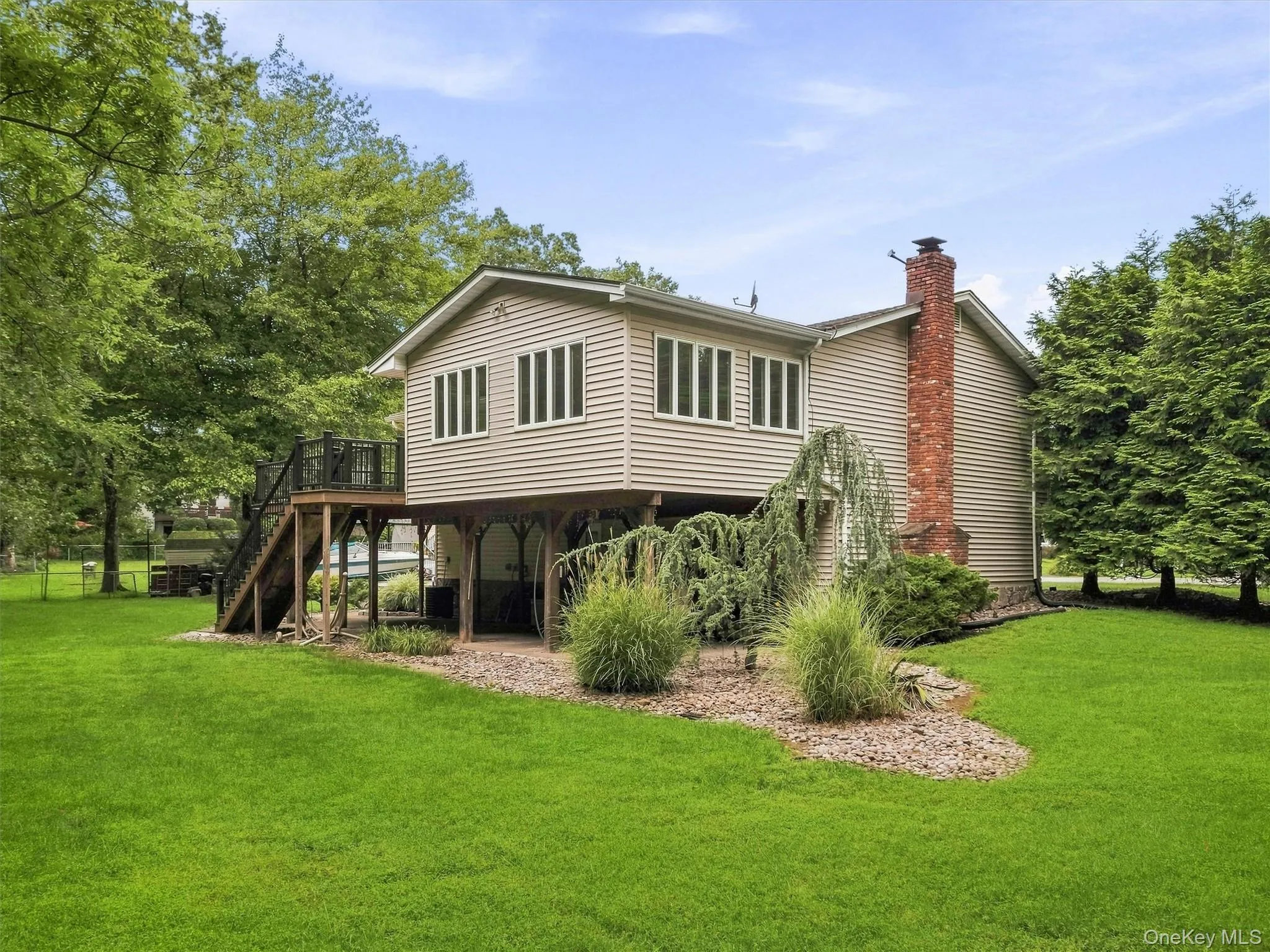 Elevated deck with dark railings, siding exterior, brick chimney, and mature landscaping Elevated deck with dark railings, siding exterior, brick chimney, and mature landscaping
