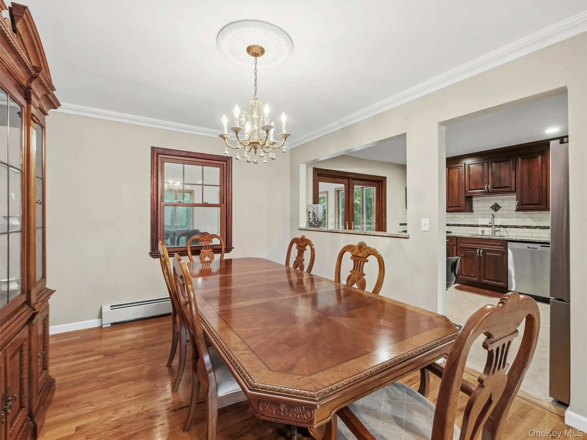 Hardwood flooring, crown molding, a decorative ceiling medallion, a brass-finish chandelier, and a kitchen pass-through with a tile backsplash Hardwood flooring, crown molding, a decorative ceiling medallion, a brass-finish chandelier, and a kitchen pass-through with a tile backsplash