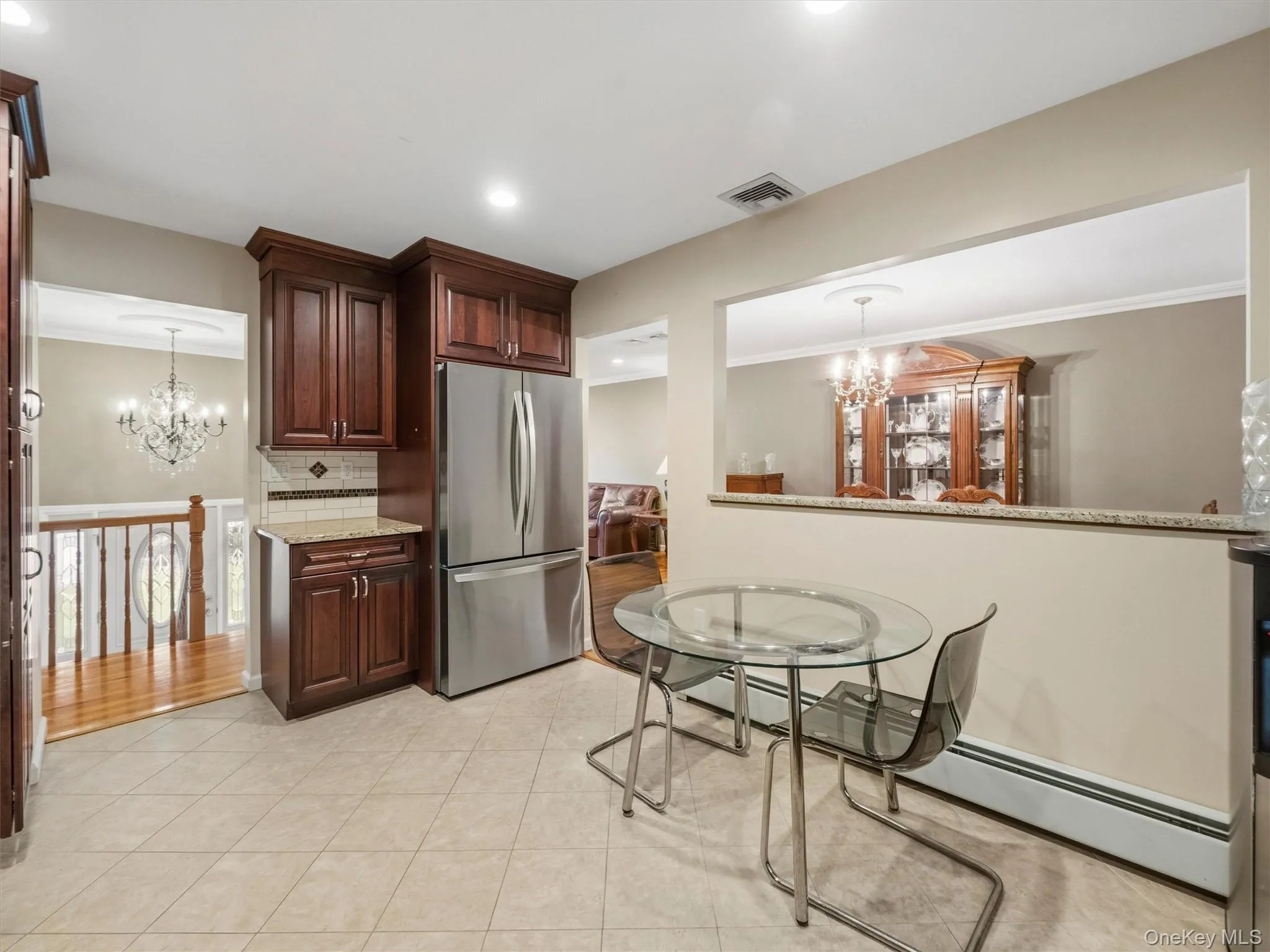 Kitchen featuring floor tile, dark wood-finish cabinetry, stainless steel refrigerator, and stone countertops Kitchen featuring floor tile, dark wood-finish cabinetry, stainless steel refrigerator, and stone countertops