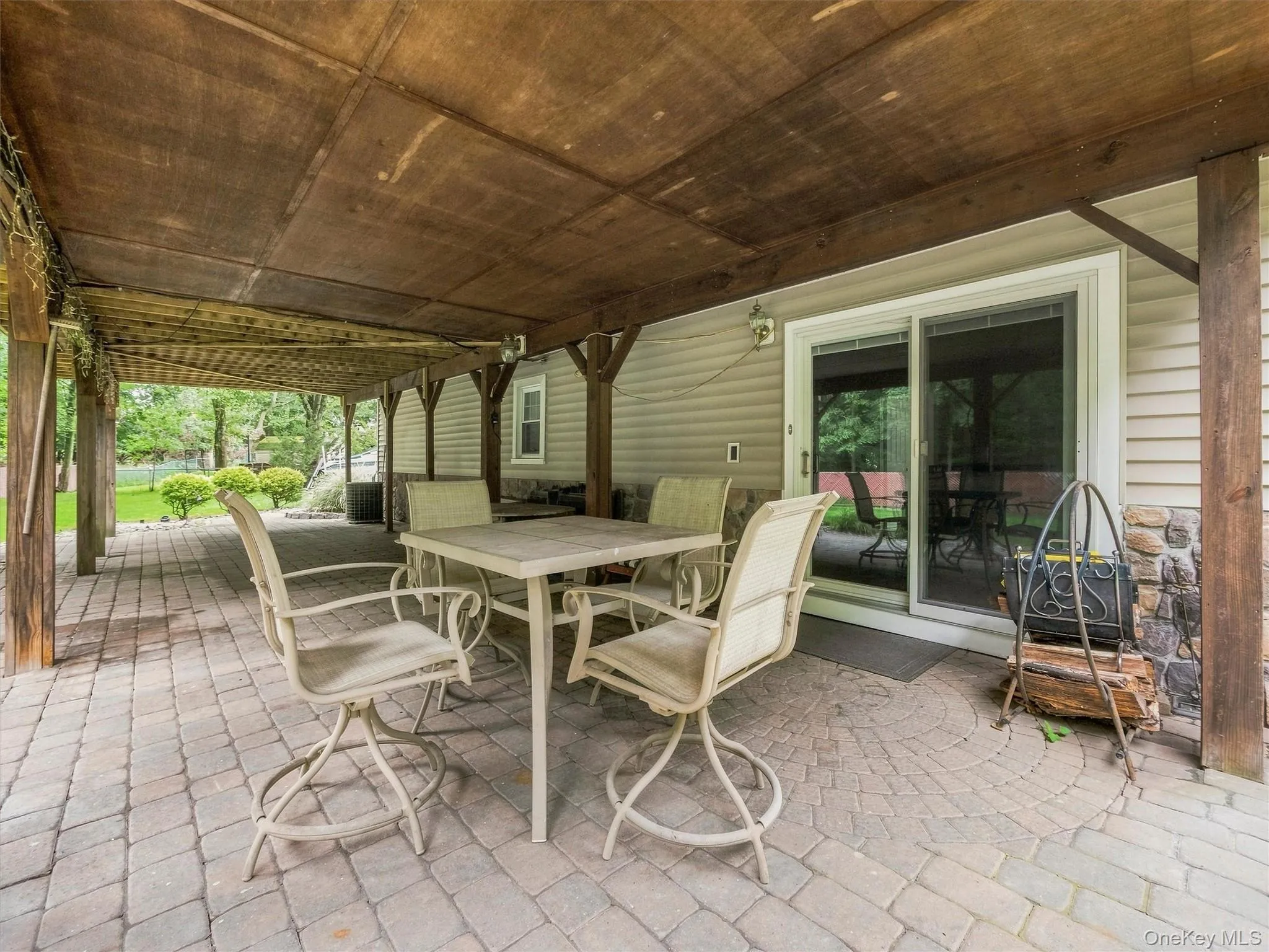 Covered patio featuring wood beam construction, paver flooring, stone column accents, and sliding glass door access Covered patio featuring wood beam construction, paver flooring, stone column accents, and sliding glass door access