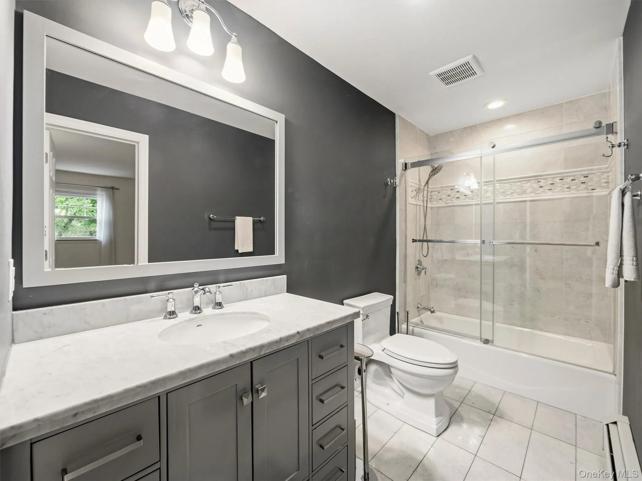 Vanity with a white countertop and undermount sink, framed mirror, three-light fixture, glass-enclosed shower, and tiled flooring Vanity with a white countertop and undermount sink, framed mirror, three-light fixture, glass-enclosed shower, and tiled flooring