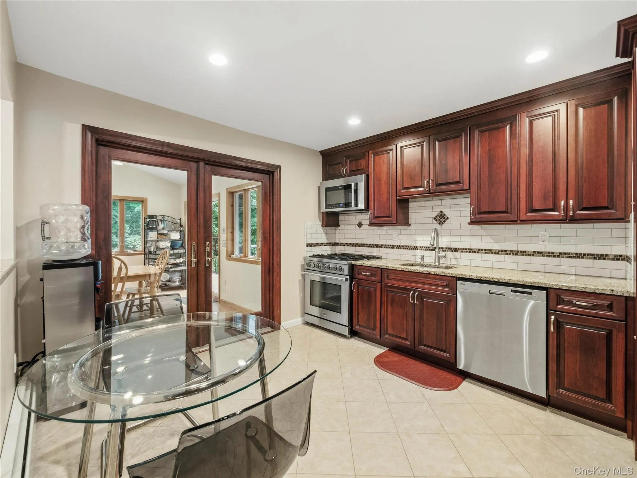Kitchen featuring wood-finish cabinetry, granite countertops, tile backsplash, and stainless steel appliances Kitchen featuring wood-finish cabinetry, granite countertops, tile backsplash, and stainless steel appliances
