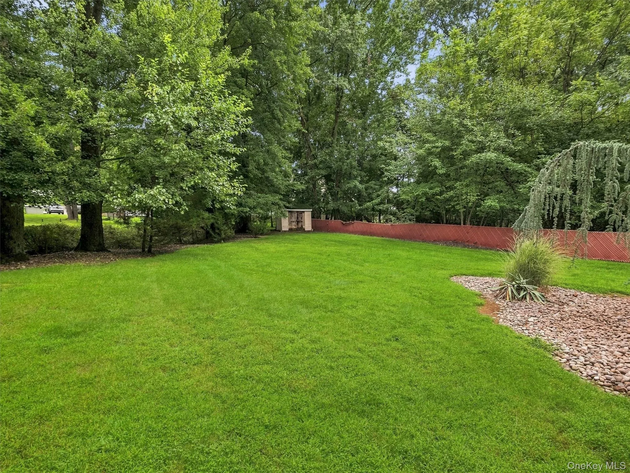 Expansive lawn area, mature trees, privacy fencing, decorative rock landscaping, and a small built structure Expansive lawn area, mature trees, privacy fencing, decorative rock landscaping, and a small built structure