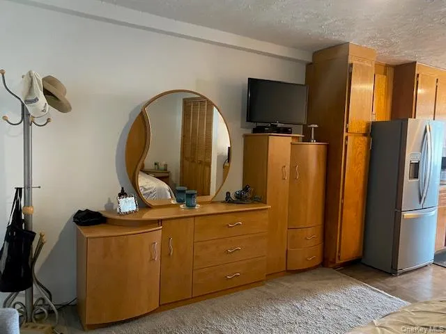 Bedroom featuring light wood-style floors, a textured ceiling, and stainless steel fridge with ice dispenser Bedroom featuring light wood-style floors, a textured ceiling, and stainless steel fridge with ice dispenser