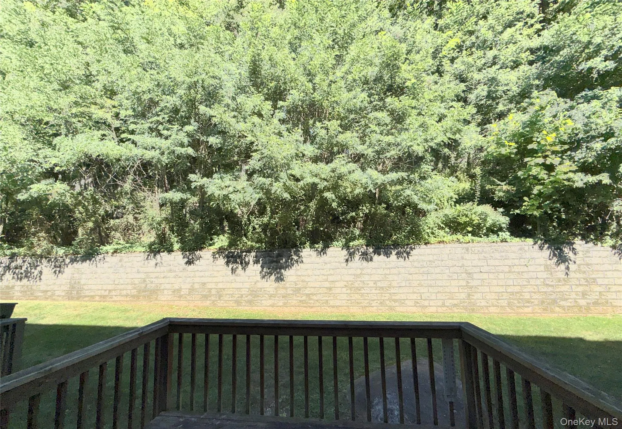 Spacious back deck facing lawn, retaining wall and tree lined property Spacious back deck facing lawn, retaining wall and tree lined property