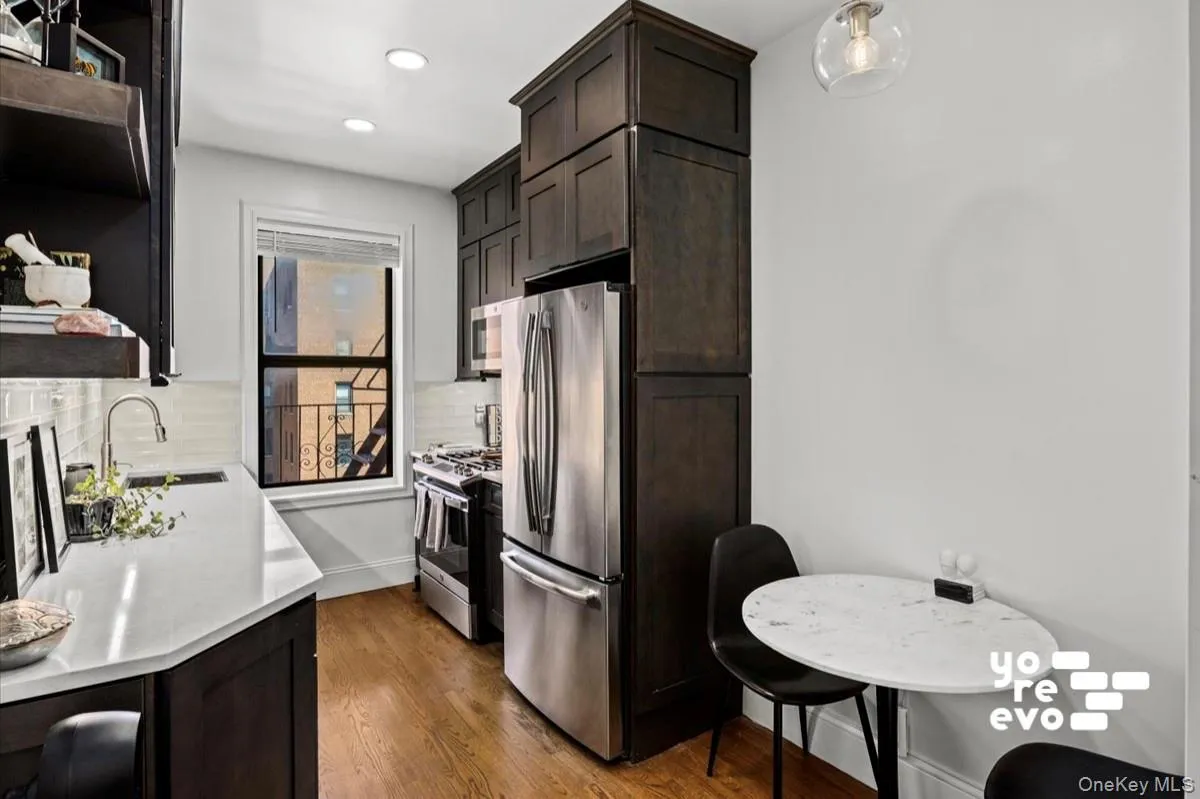 Stainless steel appliances, recessed lighting, wood-finish flooring, white subway tile backsplash, and dark wood-finish cabinetry Stainless steel appliances, recessed lighting, wood-finish flooring, white subway tile backsplash, and dark wood-finish cabinetry