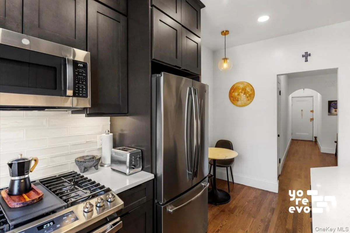 Kitchen featuring stainless steel appliances, dark wood-finish cabinetry, light stone-finish countertops, and a subway tile backsplash Kitchen featuring stainless steel appliances, dark wood-finish cabinetry, light stone-finish countertops, and a subway tile backsplash