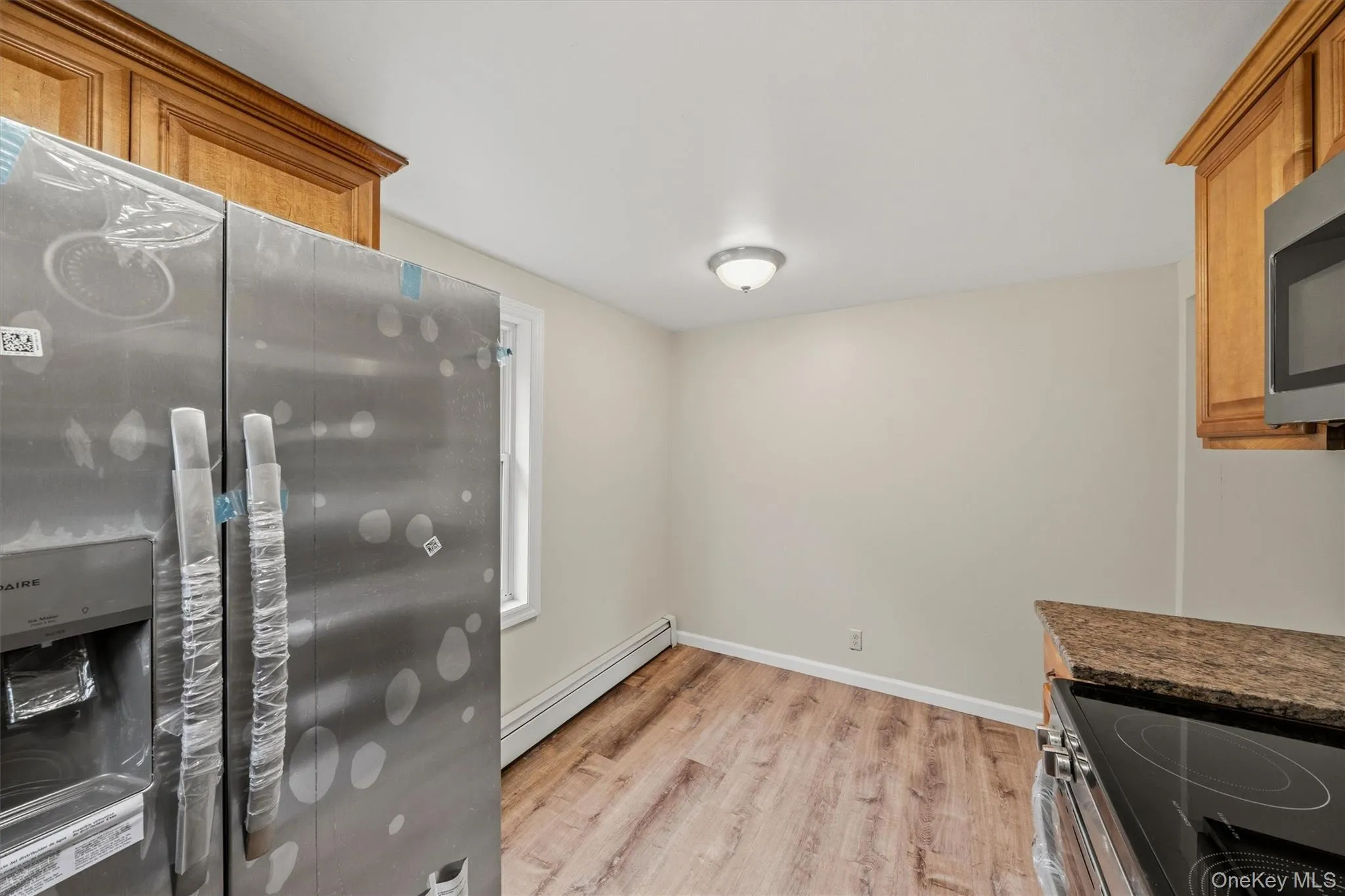 Stainless steel refrigerator, upper wood-finish cabinetry, built-in microwave, wood-finish flooring, and a window Stainless steel refrigerator, upper wood-finish cabinetry, built-in microwave, wood-finish flooring, and a window