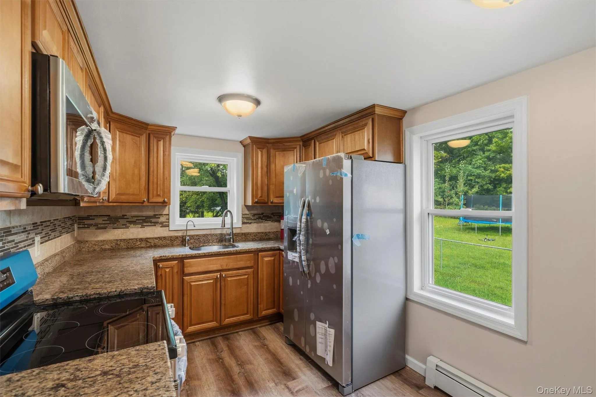 Wood-finish flooring, wood cabinetry, stone-finish countertops, stainless steel appliances, and a tile backsplash Wood-finish flooring, wood cabinetry, stone-finish countertops, stainless steel appliances, and a tile backsplash