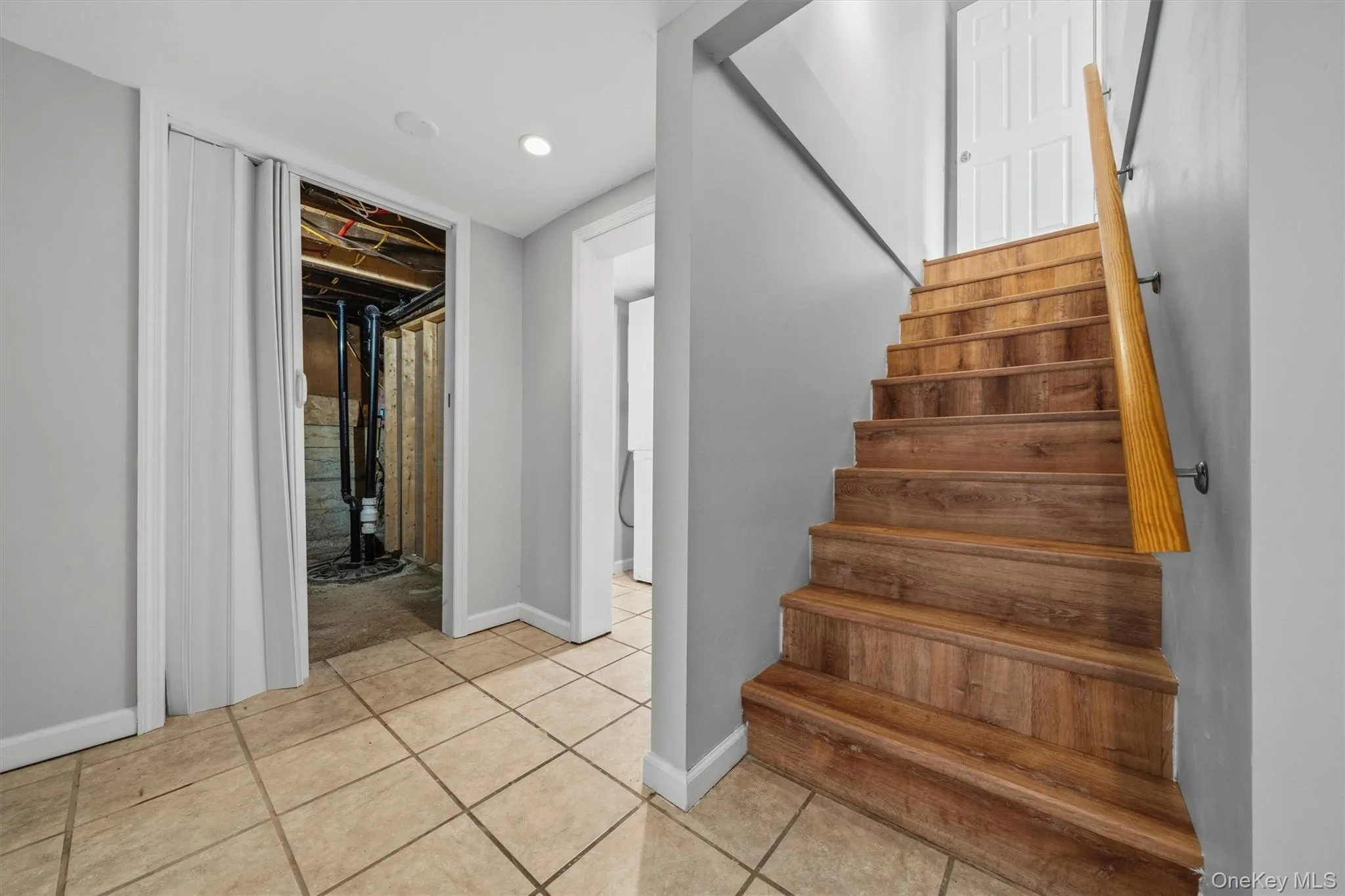 Wood-finish staircase with a wooden handrail, recessed lighting, and tile flooring Wood-finish staircase with a wooden handrail, recessed lighting, and tile flooring
