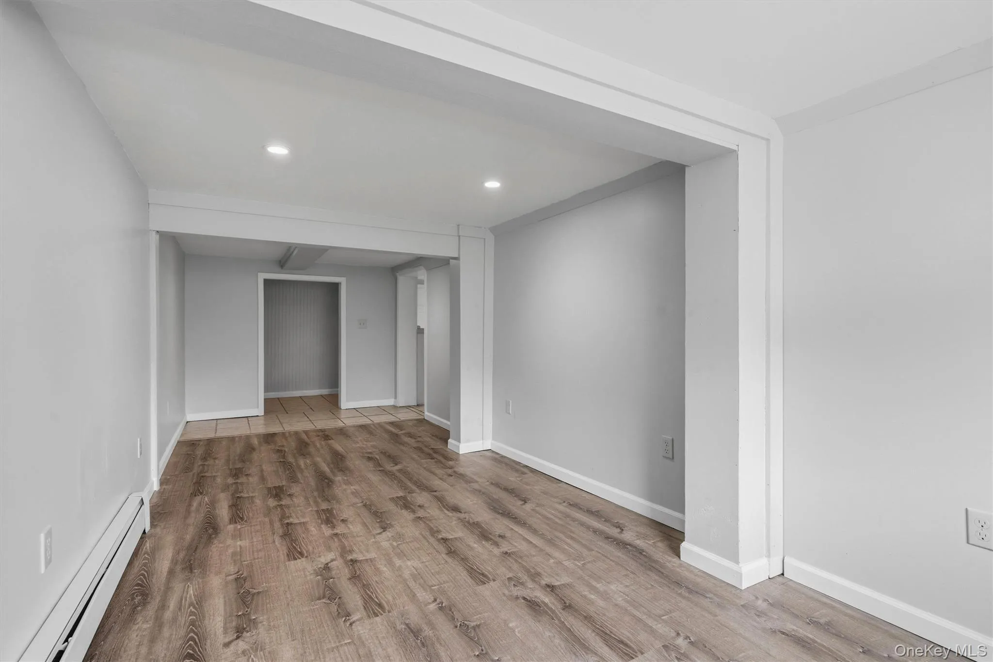 Recessed lighting, wood-finish flooring, light gray walls, white trim, and a radiator Recessed lighting, wood-finish flooring, light gray walls, white trim, and a radiator
