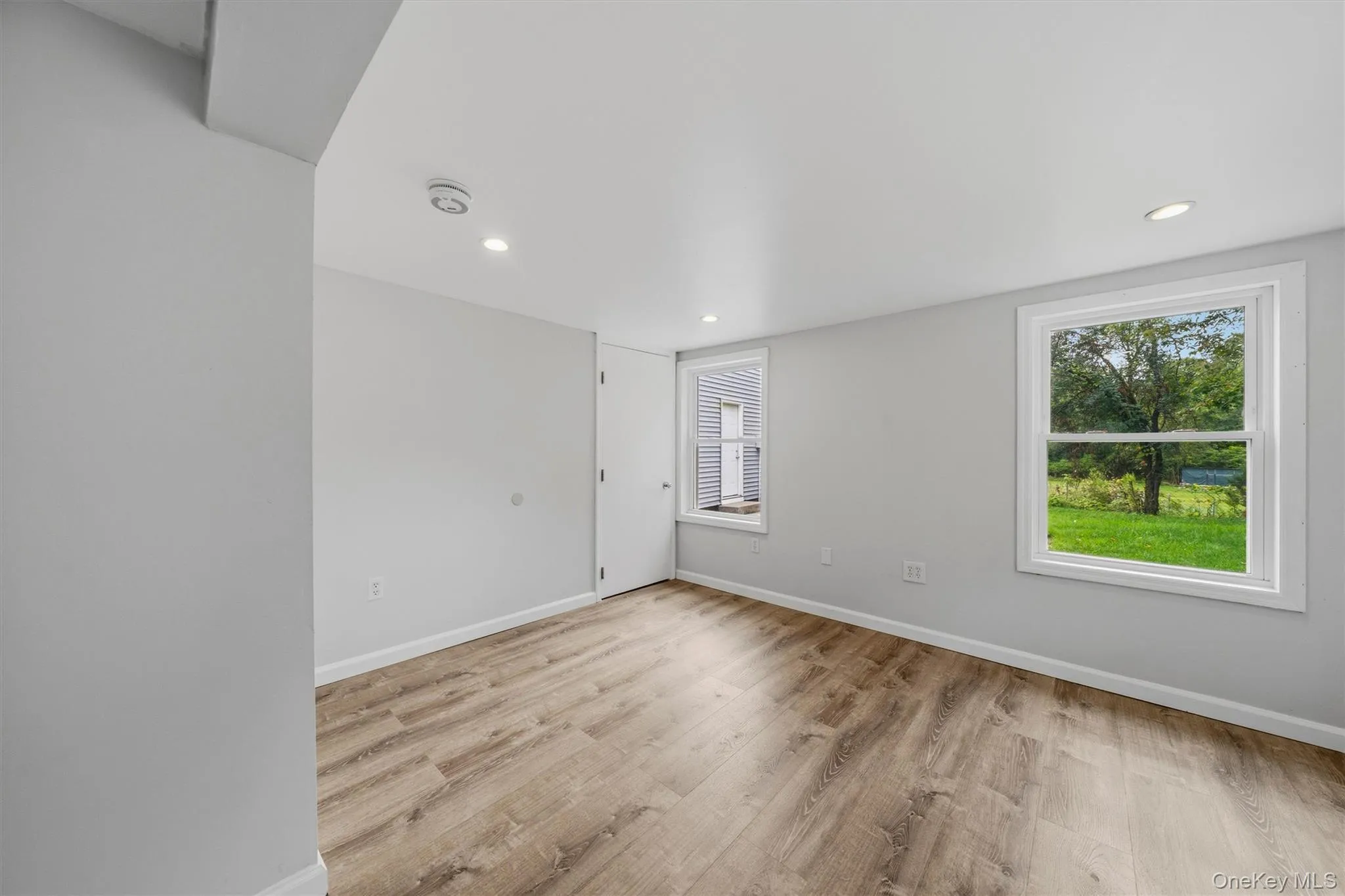 Light gray walls, recessed lighting, wood-finish flooring, and white window trim Light gray walls, recessed lighting, wood-finish flooring, and white window trim