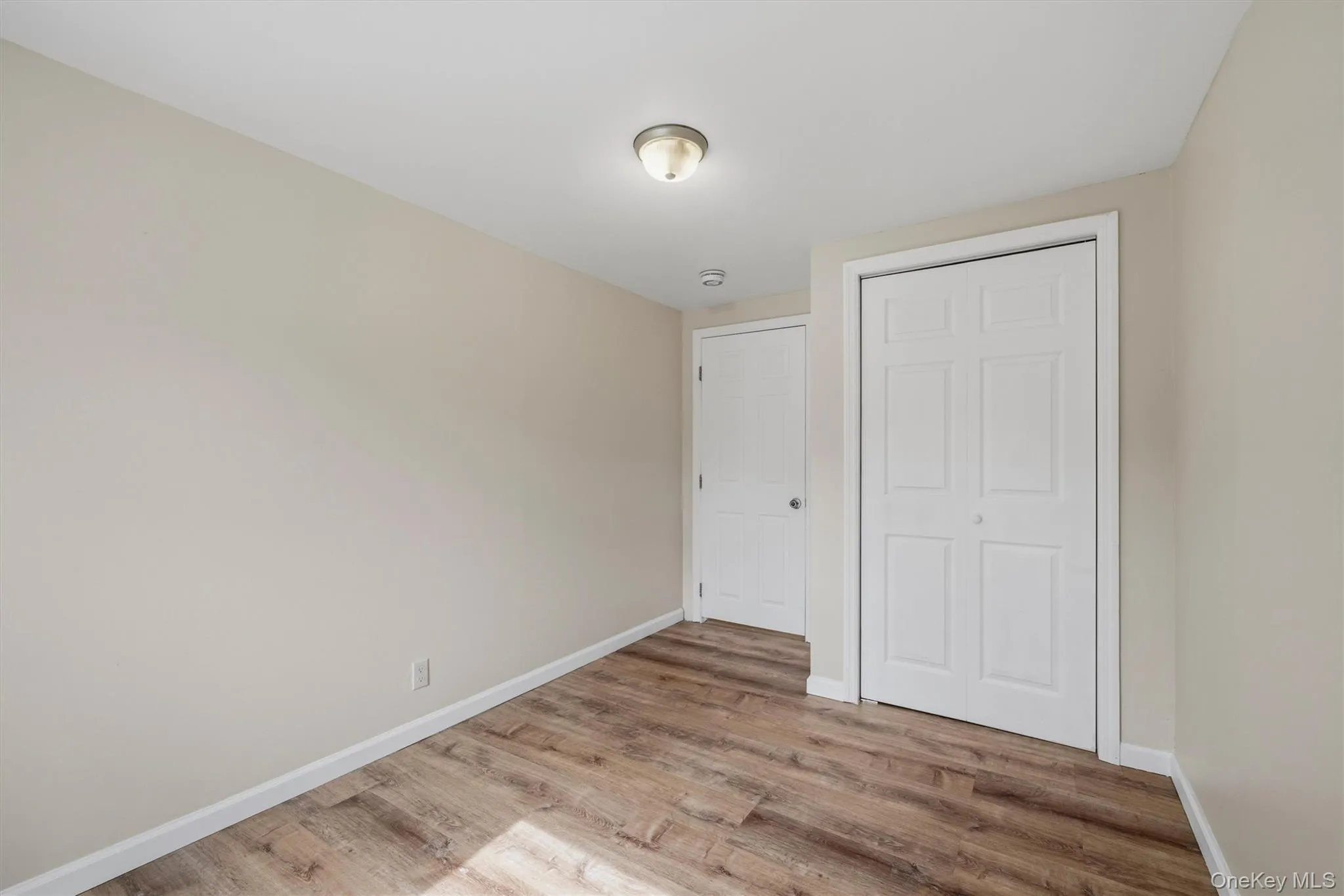 Wood-finish flooring, neutral wall tones, white trim, and a flush-mount ceiling light Wood-finish flooring, neutral wall tones, white trim, and a flush-mount ceiling light