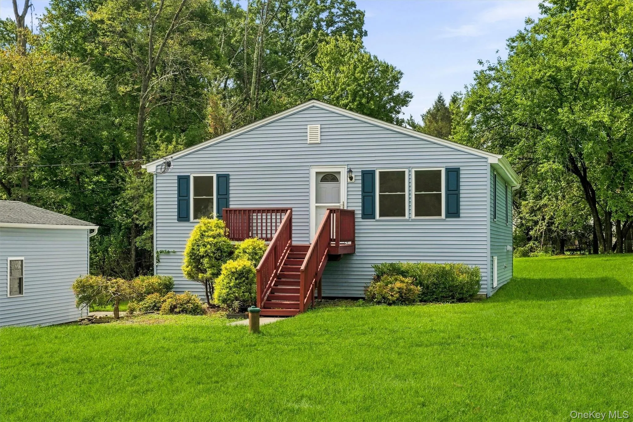 Light blue siding with dark blue shutters, elevated entrance with red wood stairs and railing, and a large front yard with mature landscaping Light blue siding with dark blue shutters, elevated entrance with red wood stairs and railing, and a large front yard with mature landscaping