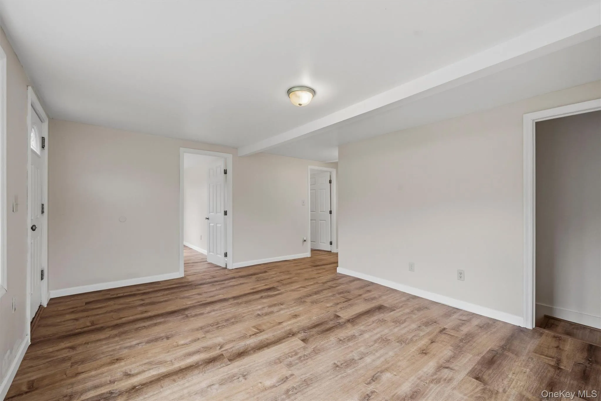 Wood-finish flooring throughout, white trim, and a ceiling-mounted light fixture Wood-finish flooring throughout, white trim, and a ceiling-mounted light fixture