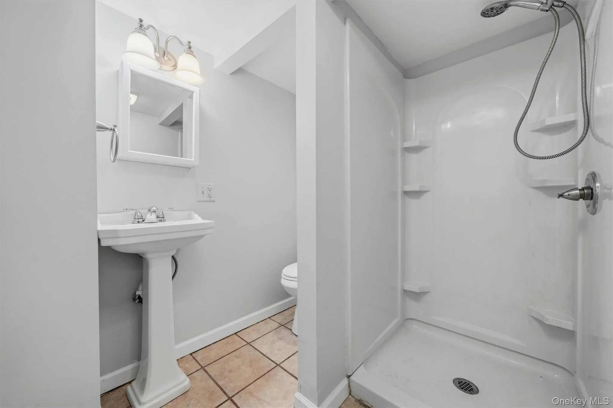 Pedestal sink with a framed mirror, overhead vanity lighting, and a walk-in shower with a handheld showerhead Pedestal sink with a framed mirror, overhead vanity lighting, and a walk-in shower with a handheld showerhead