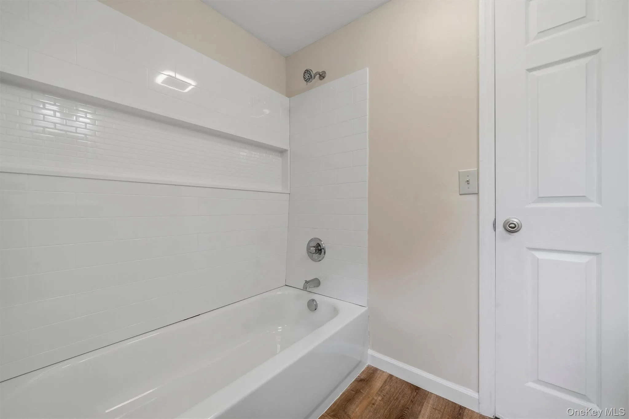 Bathtub with subway tile surround, integrated shelf, and wood-finish flooring Bathtub with subway tile surround, integrated shelf, and wood-finish flooring