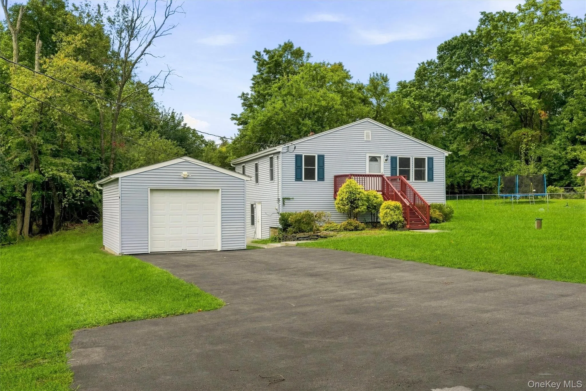 Light blue siding exterior with dark blue window shutters, red-painted deck, attached single-car garage, expansive green lawn, and mature trees Light blue siding exterior with dark blue window shutters, red-painted deck, attached single-car garage, expansive green lawn, and mature trees
