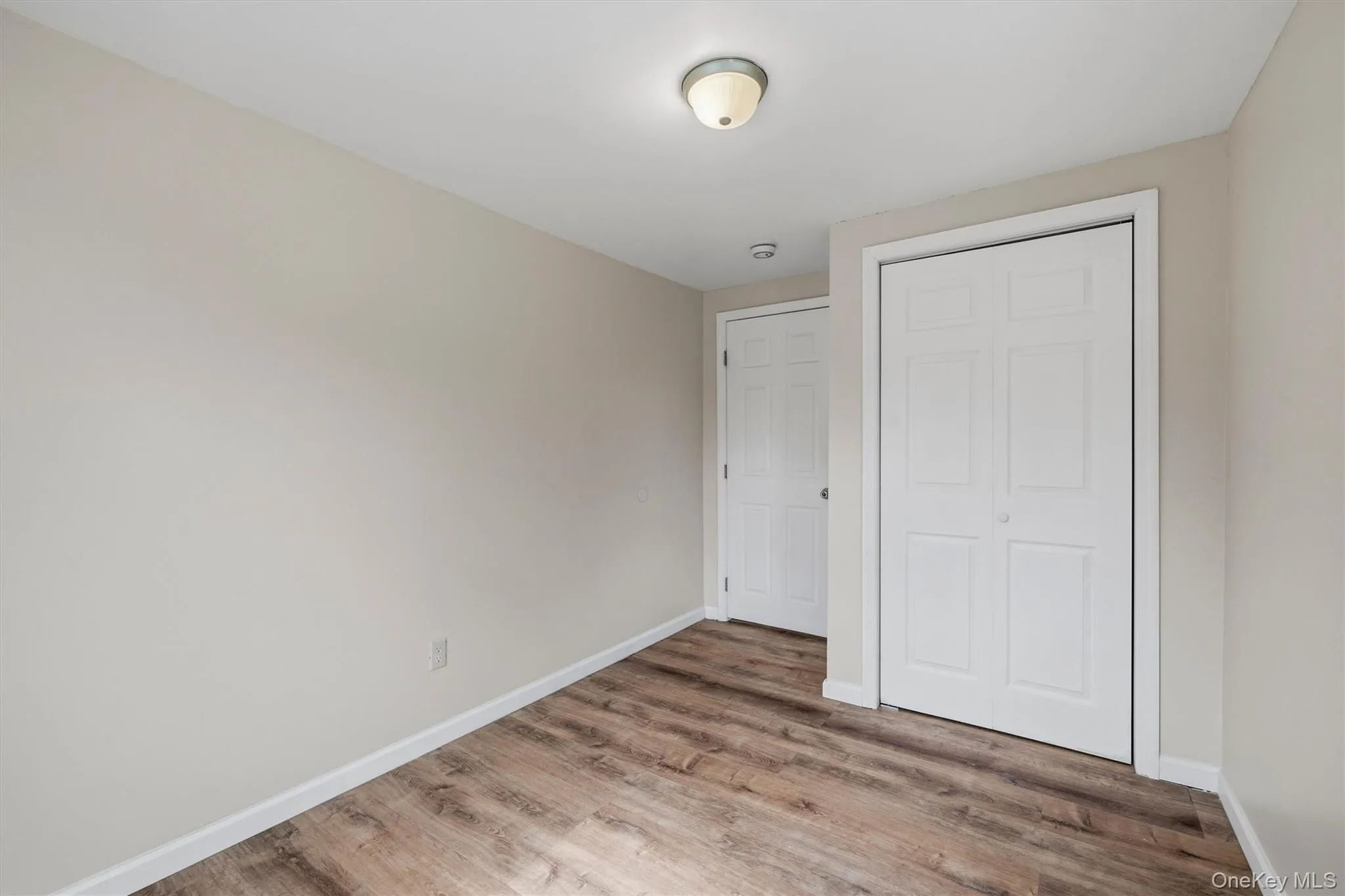 Wood-finish flooring, neutral wall tones, white trim, and a flush mount ceiling light Wood-finish flooring, neutral wall tones, white trim, and a flush mount ceiling light