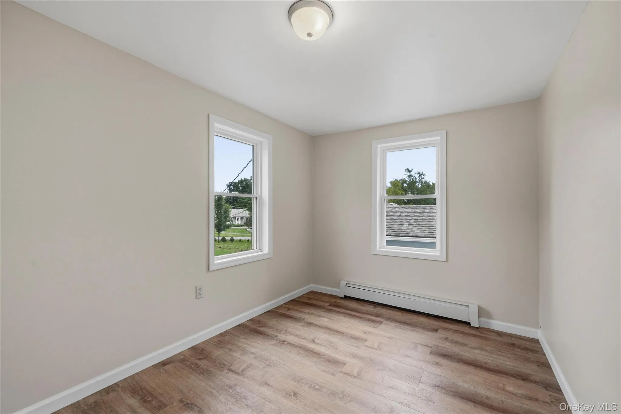 Wood-finish flooring, neutral wall tones, white trim, and a ceiling-mounted light fixture Wood-finish flooring, neutral wall tones, white trim, and a ceiling-mounted light fixture