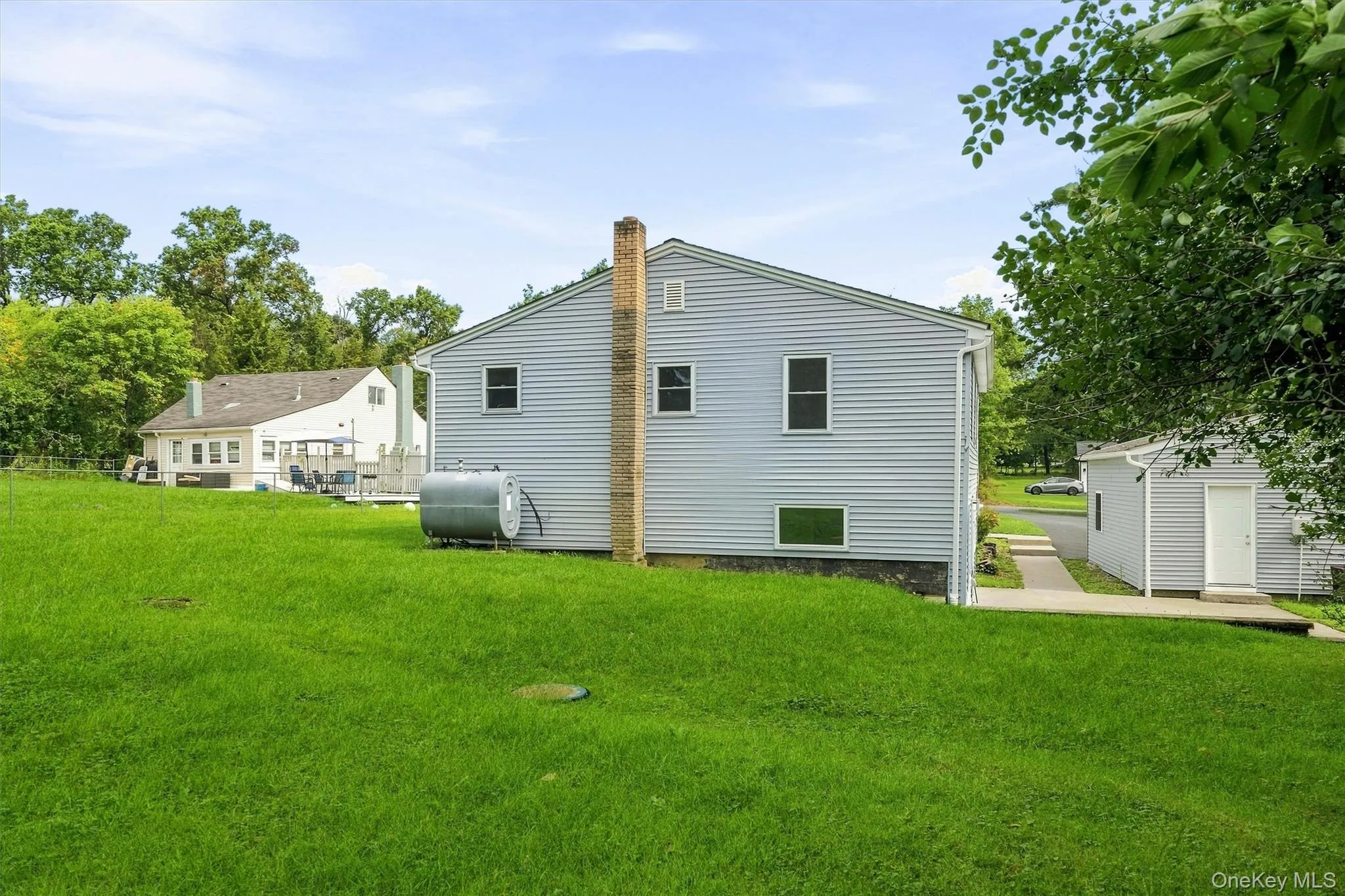 Expansive green space featuring a detached storage shed, a paved pathway, and mature trees Expansive green space featuring a detached storage shed, a paved pathway, and mature trees