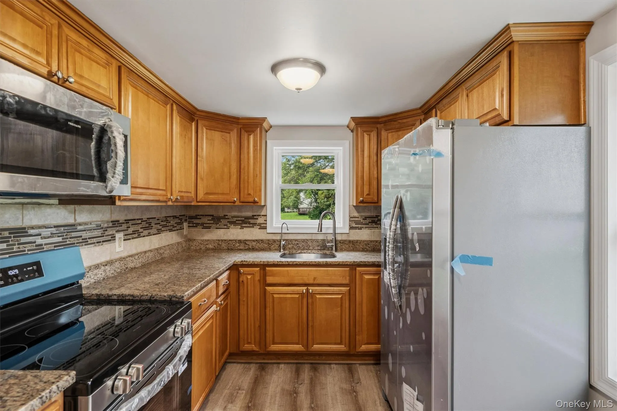 Kitchen featuring wood-finish cabinetry, stainless steel appliances, mosaic tile backsplash, and wood-finish flooring Kitchen featuring wood-finish cabinetry, stainless steel appliances, mosaic tile backsplash, and wood-finish flooring
