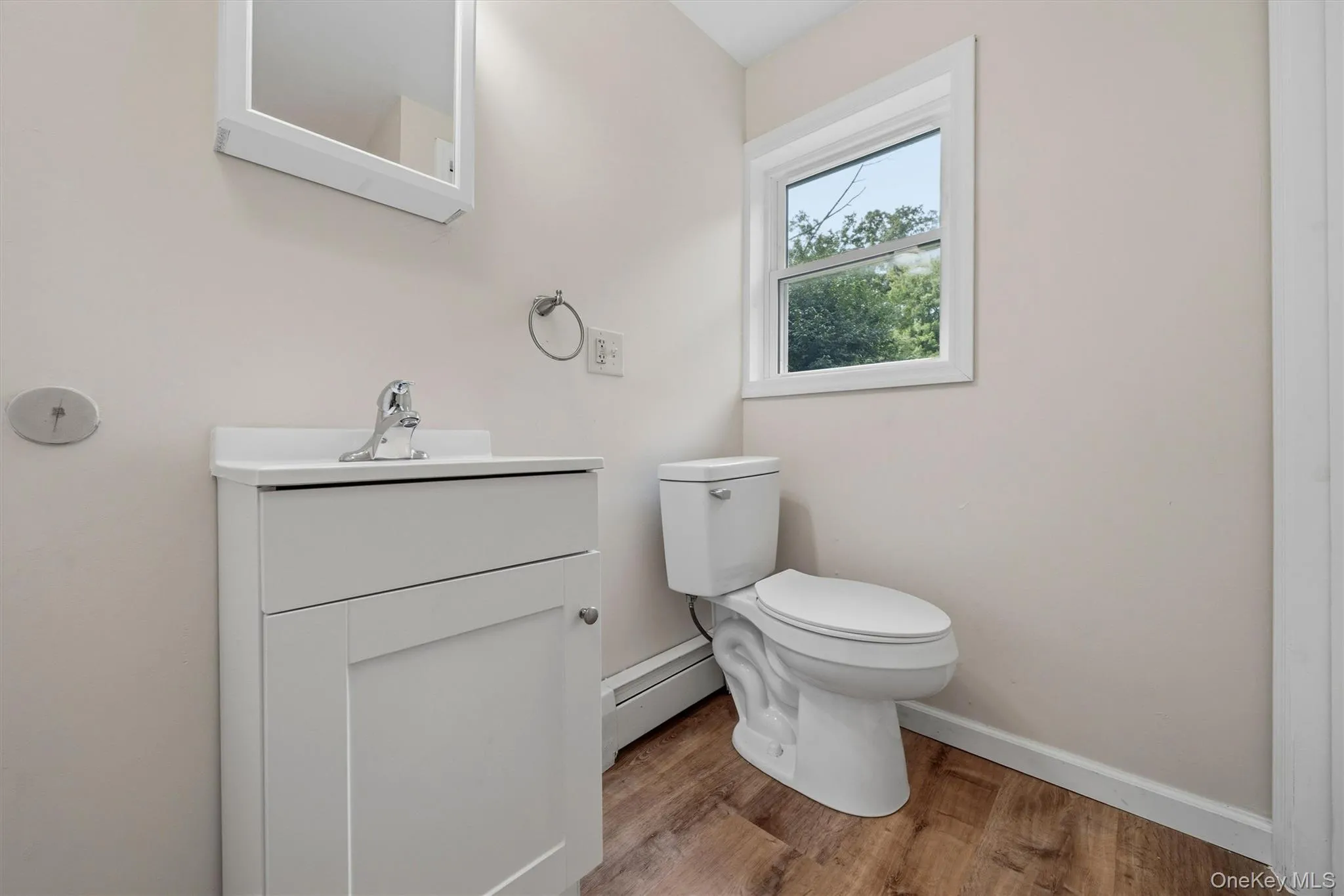 White vanity with integrated sink, chrome faucet, wood-finish flooring, and a single window White vanity with integrated sink, chrome faucet, wood-finish flooring, and a single window