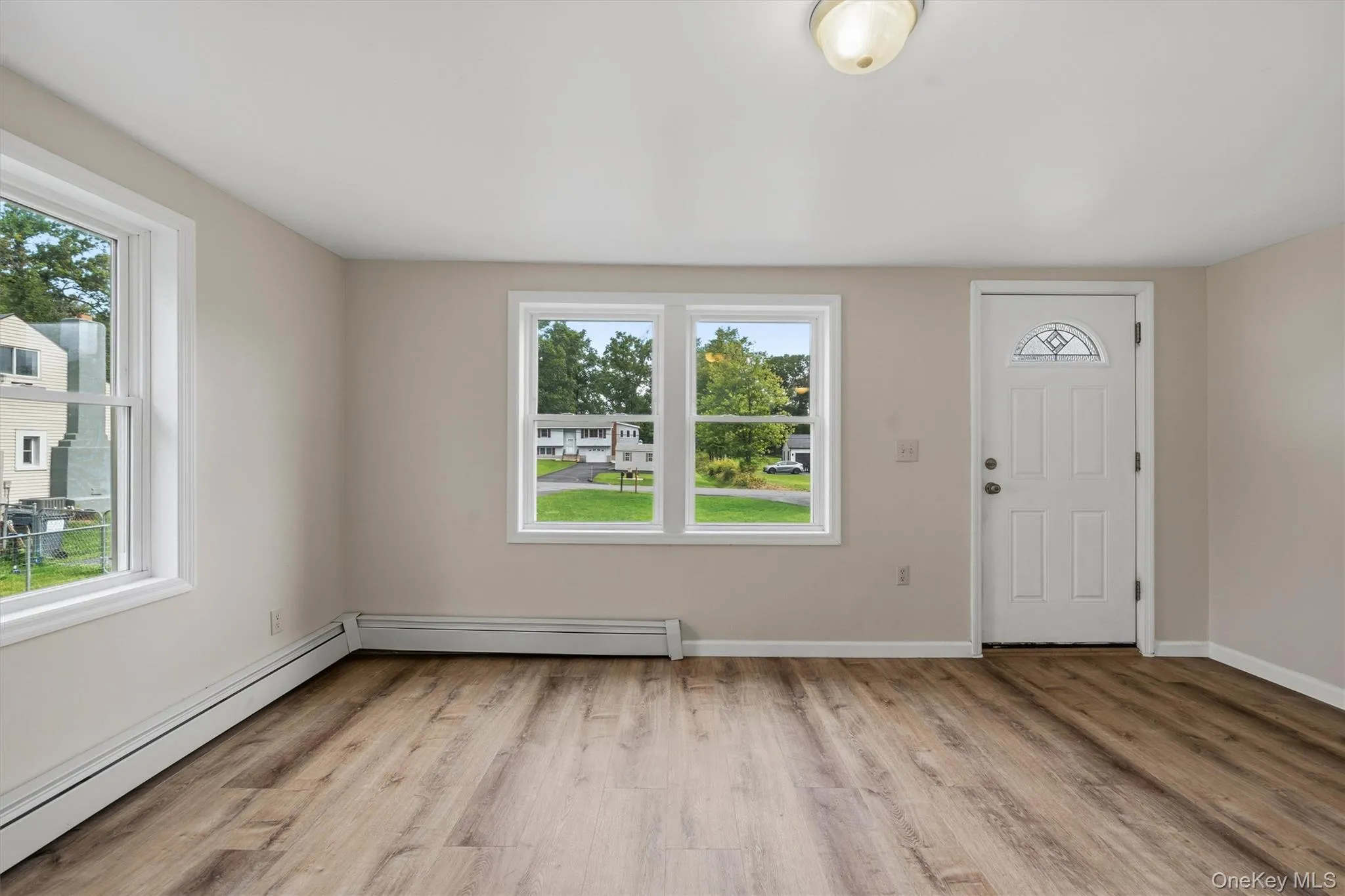 Wood-finish flooring, multiple windows with white trim, a white paneled entry door with decorative glass, and a ceiling-mounted light fixture Wood-finish flooring, multiple windows with white trim, a white paneled entry door with decorative glass, and a ceiling-mounted light fixture
