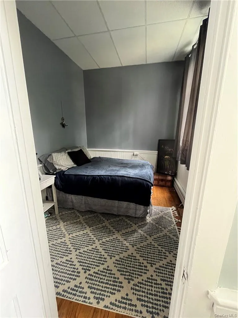 Bedroom with hardwood wood floors, a baseboard radiator, and a drop ceiling Bedroom with hardwood wood floors, a baseboard radiator, and a drop ceiling