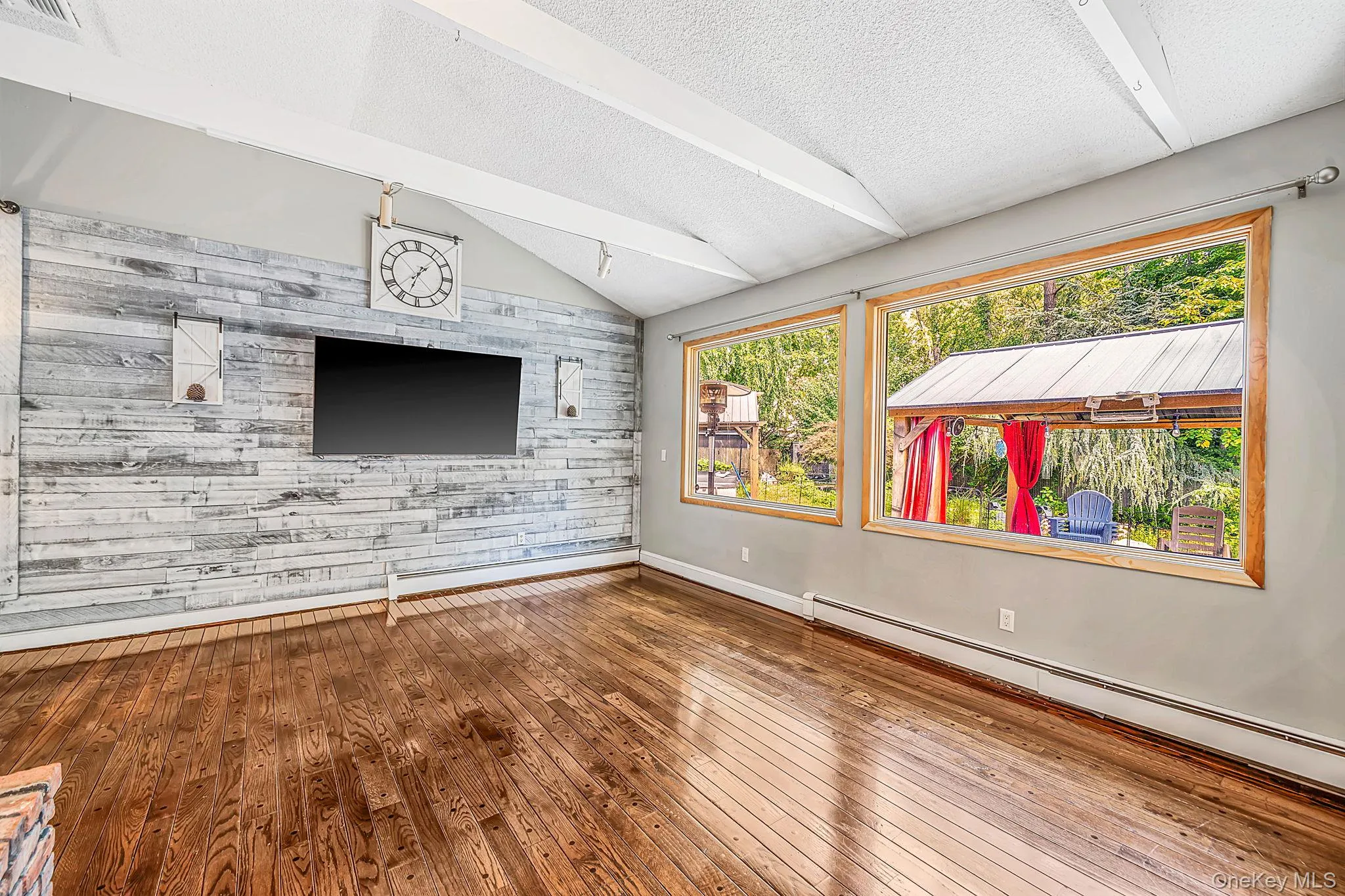 Vaulted ceiling with exposed beams, wood-finish flooring, accent wall with horizontal wood paneling, and large windows with wood trim Vaulted ceiling with exposed beams, wood-finish flooring, accent wall with horizontal wood paneling, and large windows with wood trim