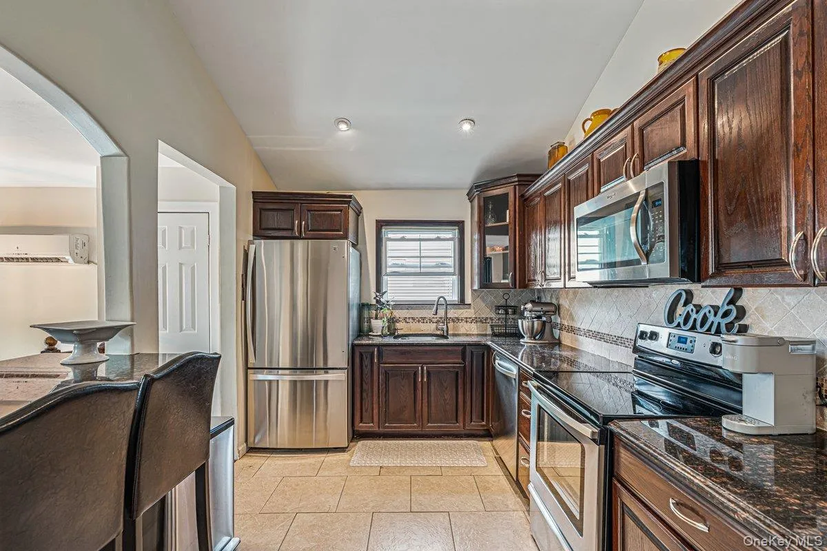 Kitchen featuring stainless steel appliances, dark wood cabinetry, granite-style countertops, and tiled flooring Kitchen featuring stainless steel appliances, dark wood cabinetry, granite-style countertops, and tiled flooring