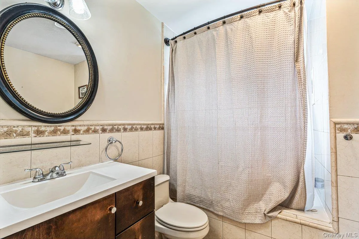 Bathroom featuring a wood-finish vanity with an integrated sink, polished chrome faucet, and decorative tile wainscoting Bathroom featuring a wood-finish vanity with an integrated sink, polished chrome faucet, and decorative tile wainscoting
