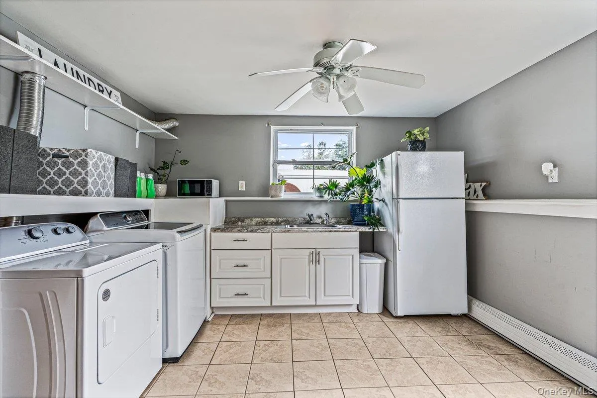 Utility room featuring tiled flooring, white built-in cabinetry, a ceiling fan, and a single window Utility room featuring tiled flooring, white built-in cabinetry, a ceiling fan, and a single window
