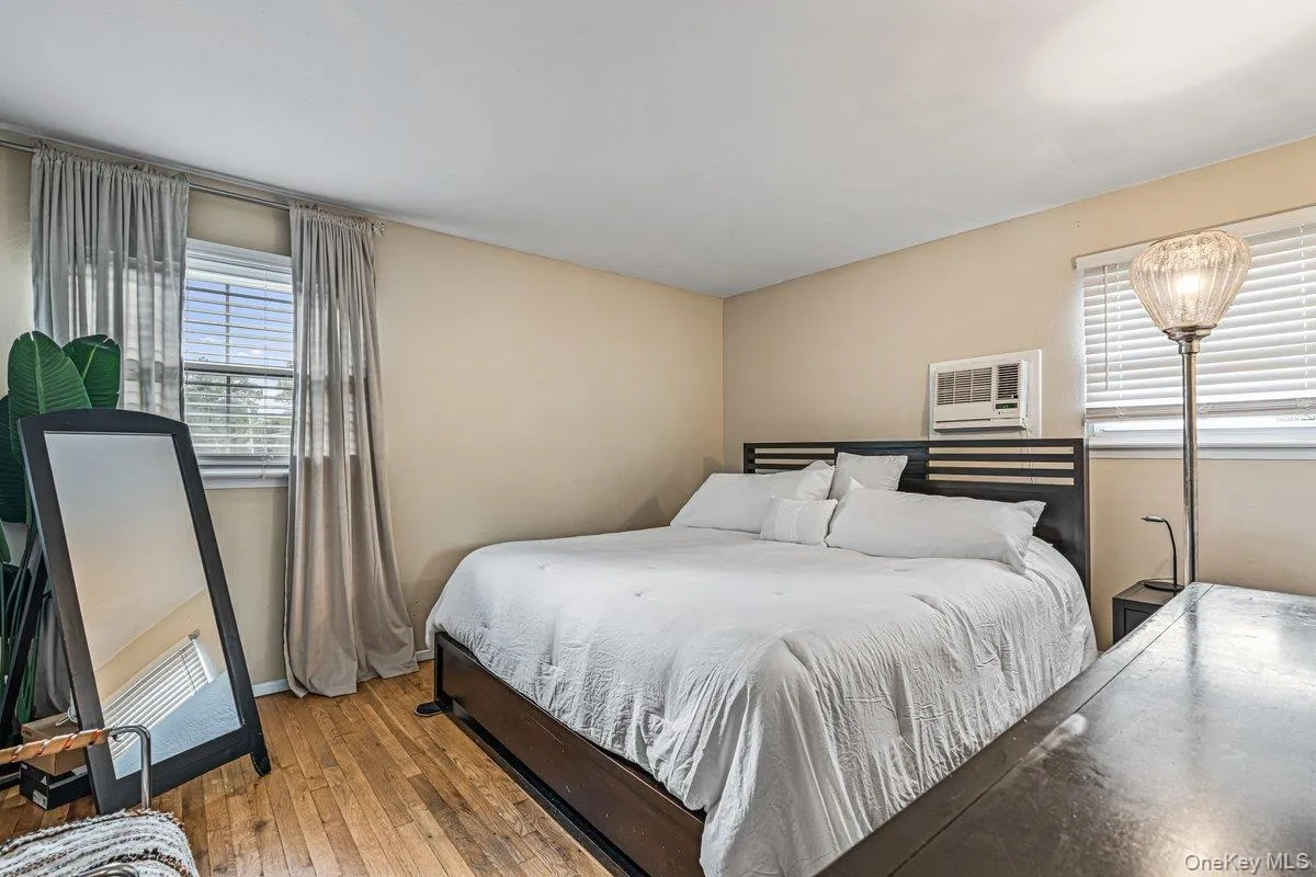 Wood-finish flooring with two windows, horizontal blinds, and a wall-mounted AC unit Wood-finish flooring with two windows, horizontal blinds, and a wall-mounted AC unit