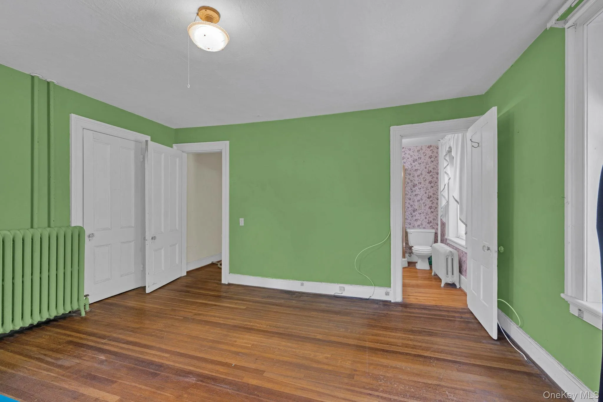 Unfurnished bedroom with radiator heating unit, dark wood-style floors, and ensuite bathroom Unfurnished bedroom with radiator heating unit, dark wood-style floors, and ensuite bathroom