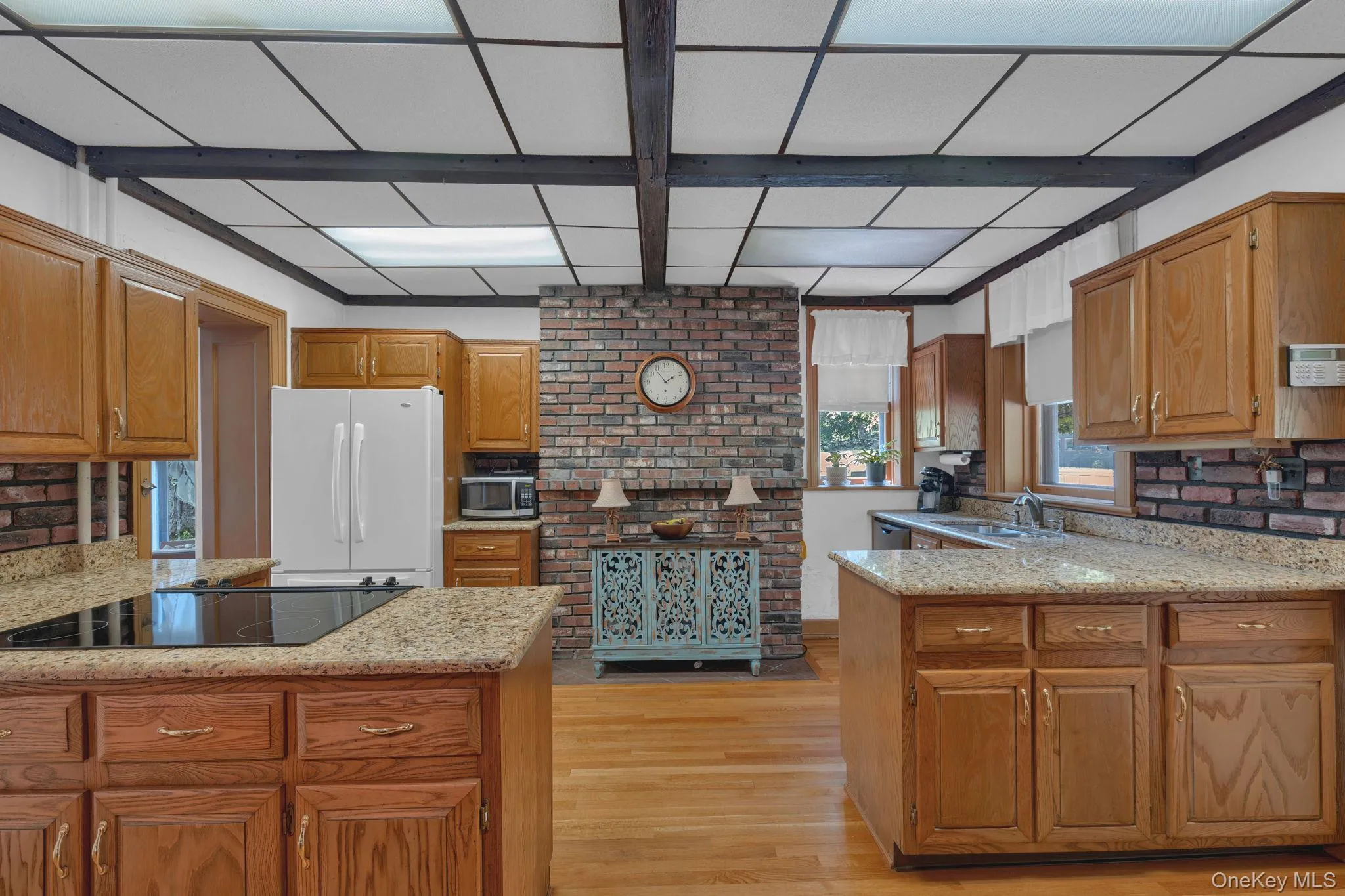 Kitchen featuring a peninsula, light wood-style flooring, light stone countertops, freestanding refrigerator, and beamed ceiling Kitchen featuring a peninsula, light wood-style flooring, light stone countertops, freestanding refrigerator, and beamed ceiling