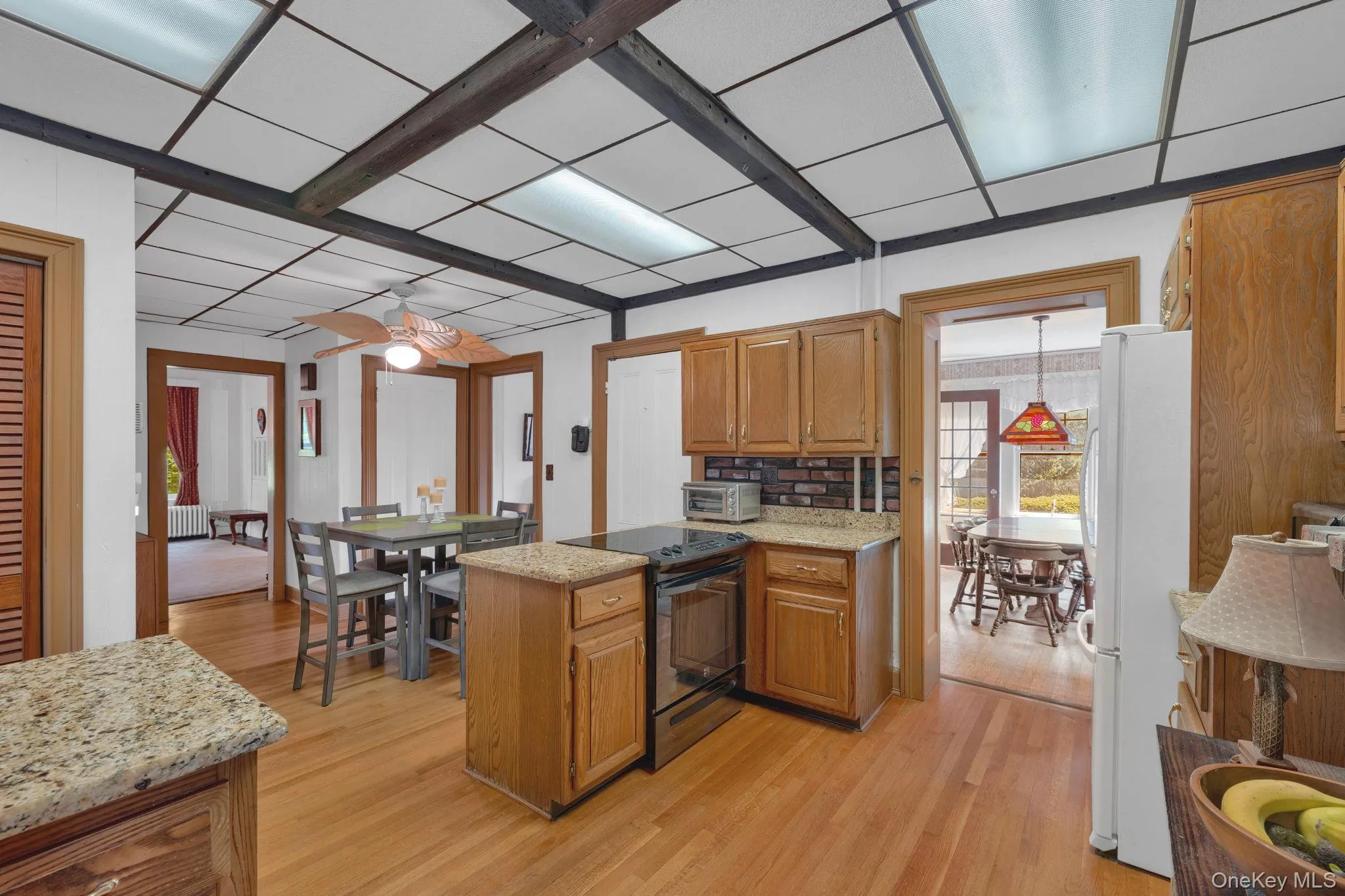 Kitchen with black range oven, light wood-style flooring, brown cabinetry, light stone counters, and freestanding refrigerator Kitchen with black range oven, light wood-style flooring, brown cabinetry, light stone counters, and freestanding refrigerator