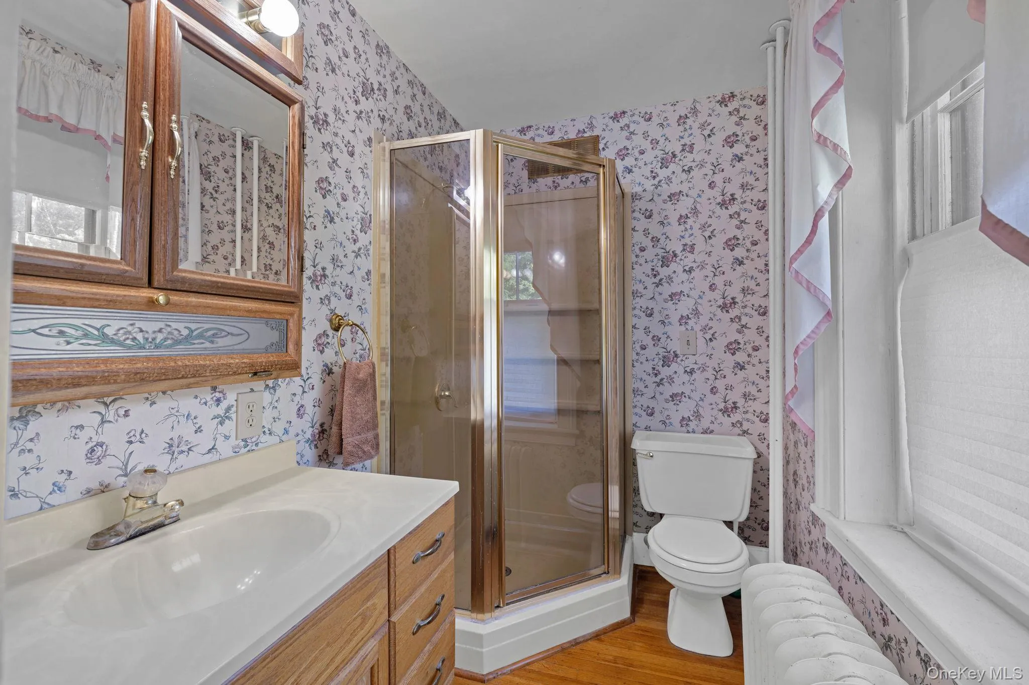 Bathroom with radiator, light wood-style floors, vanity, a stall shower, and wallpapered walls Bathroom with radiator, light wood-style floors, vanity, a stall shower, and wallpapered walls
