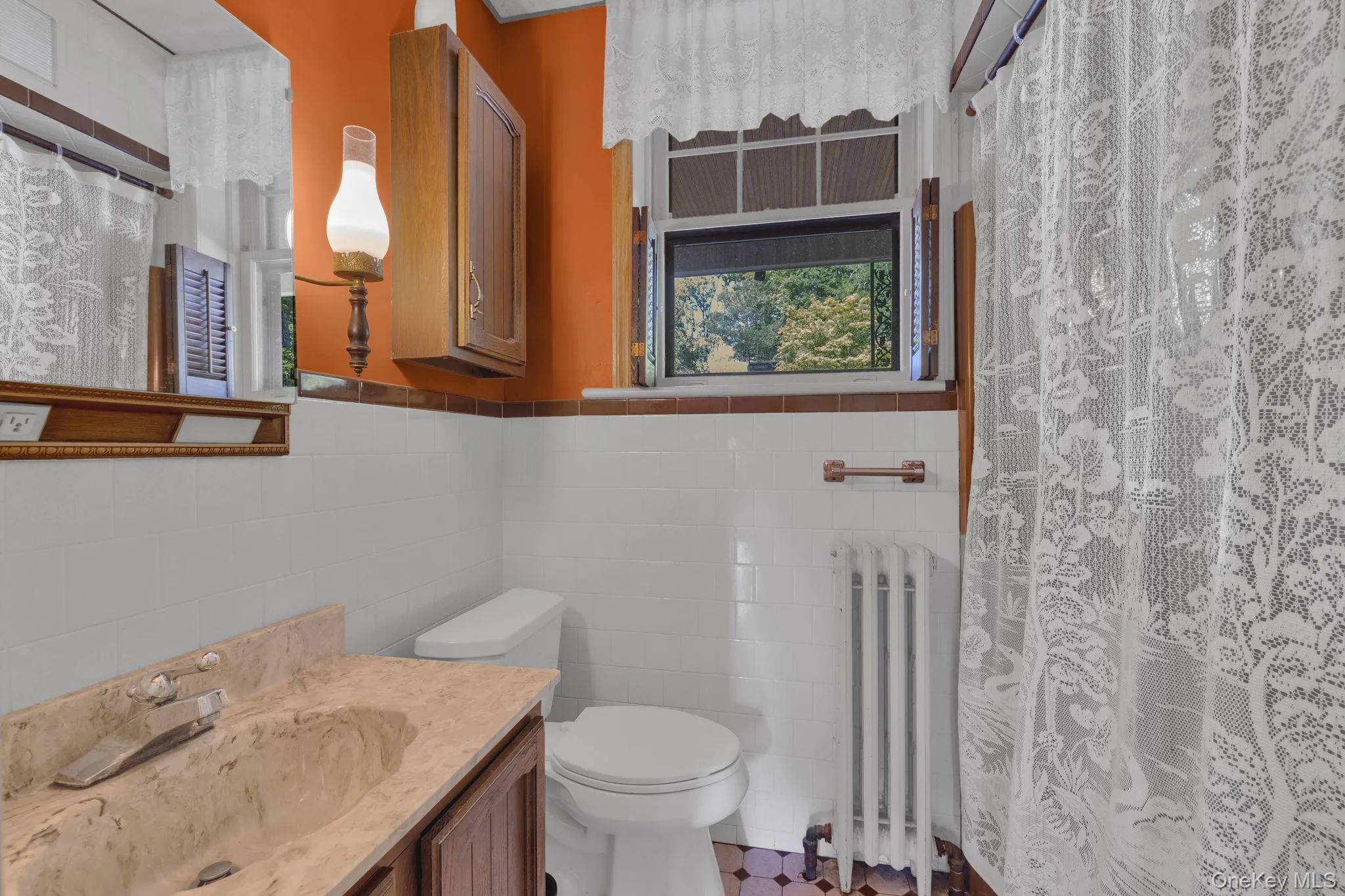 Bathroom featuring tile walls, radiator, vanity, a shower with shower curtain, and wainscoting Bathroom featuring tile walls, radiator, vanity, a shower with shower curtain, and wainscoting