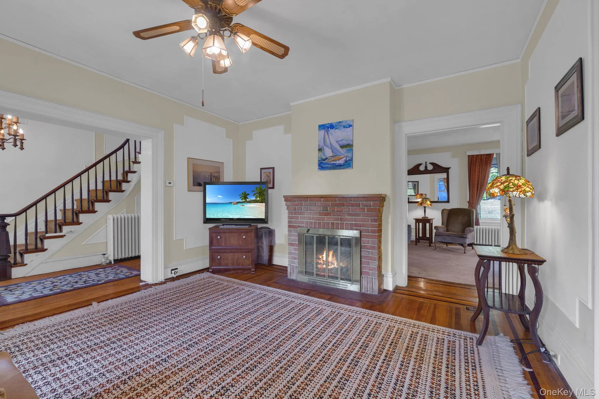 Living room featuring wood finished floors, crown molding, radiator, a fireplace, and stairs Living room featuring wood finished floors, crown molding, radiator, a fireplace, and stairs