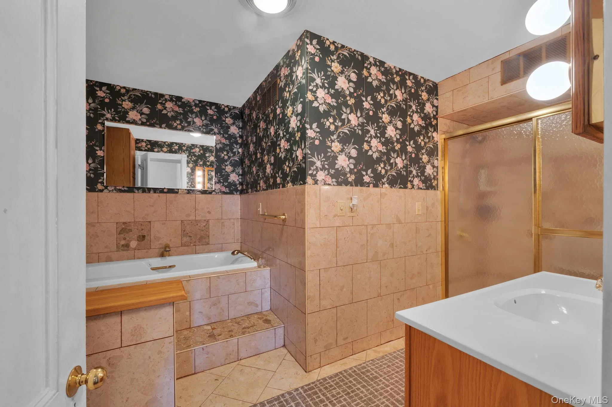 Full bath featuring tile patterned floors, tile walls, vanity, a stall shower, and a garden tub Full bath featuring tile patterned floors, tile walls, vanity, a stall shower, and a garden tub